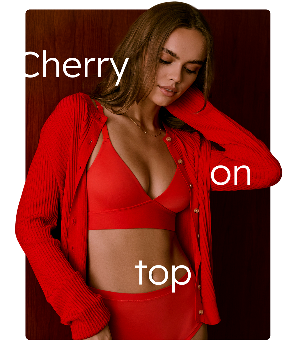 A woman in a red bra and underwear set and a red cardigan posing against a wooden background with the caption 'Cherry on top' overlayed.