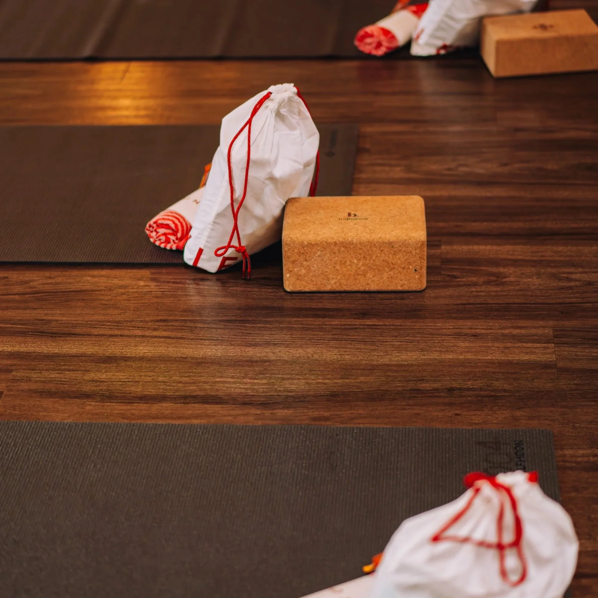 Yoga mats with white bags and cork yoga blocks on a wooden floor.