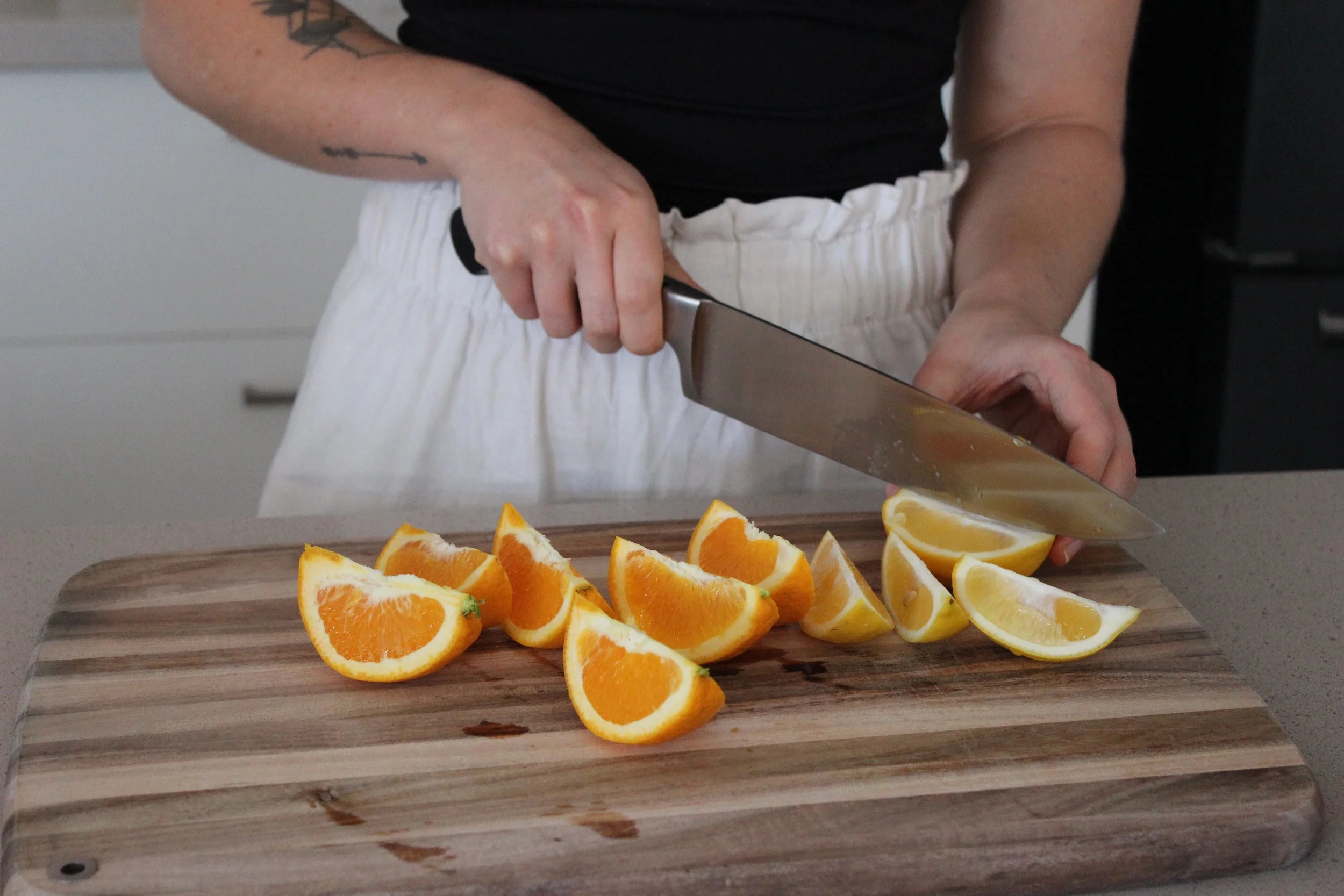 Person slicing oranges and lemons on a wooden cutting board.