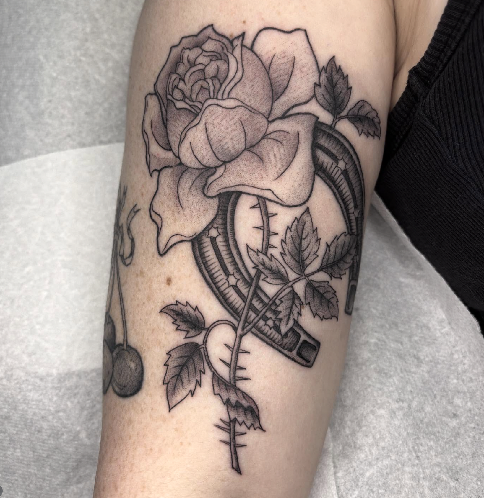 Black and gray tattoo of a rose and leaves intertwined with a pocket knife with a serrated edge.