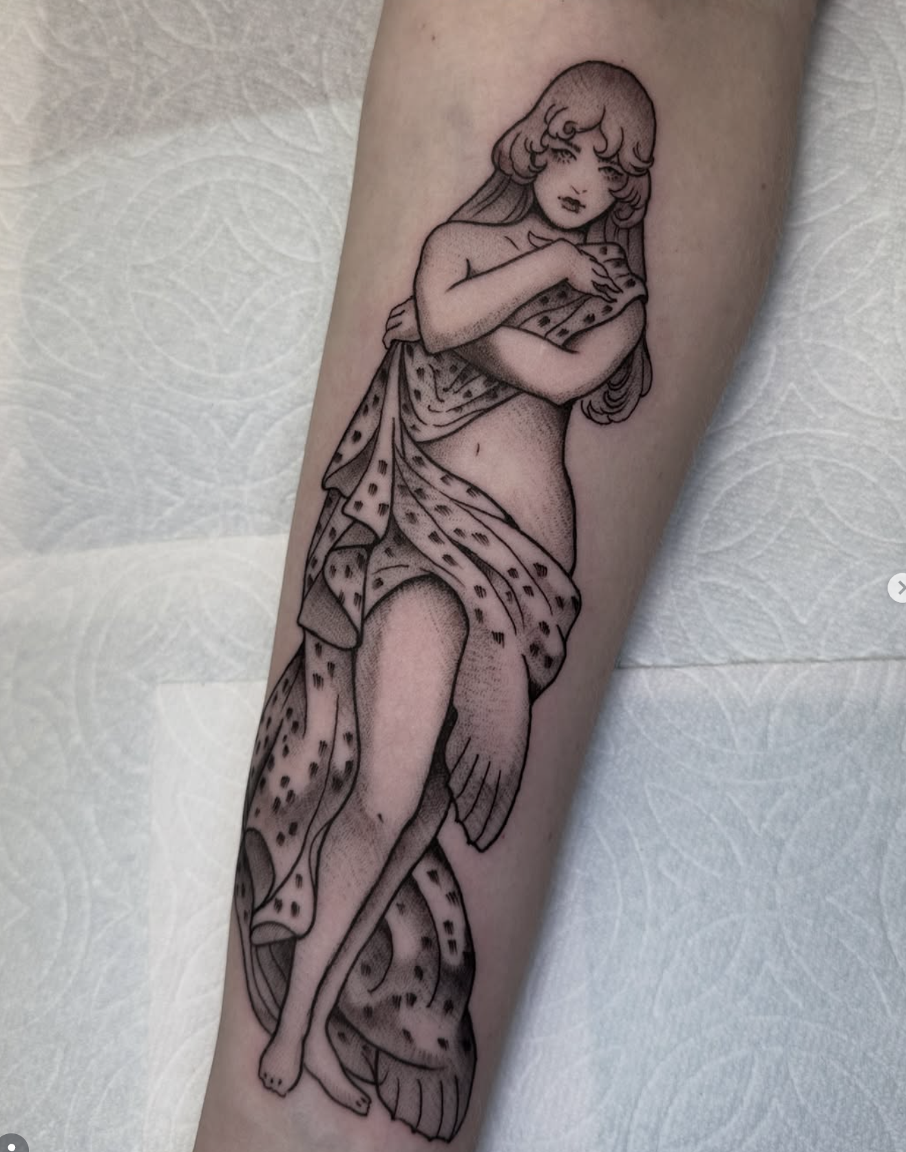 Black and gray tattoo of a woman with long hair, hugging a leopard print fabric, standing on a fish.