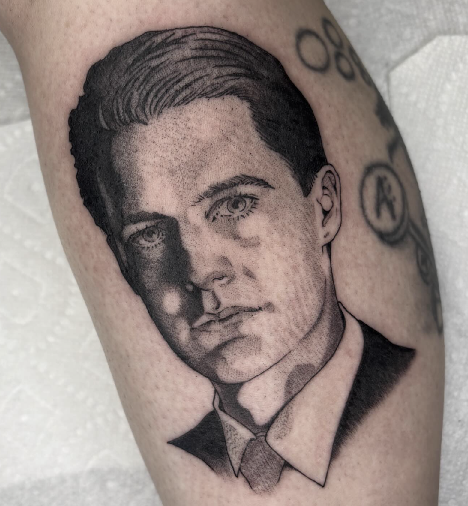 Black and gray tattoo of a young man with styled hair, wearing a collared shirt and tie.