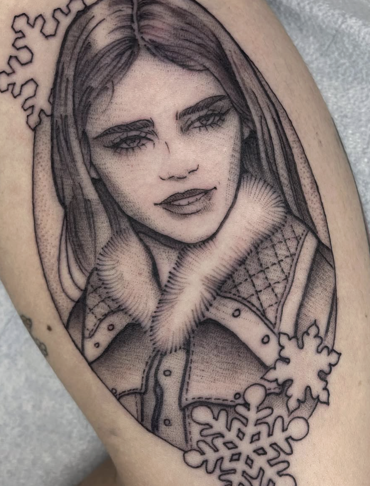 Black and gray tattoo of a woman's portrait with detailed shading, surrounded by snowflake designs.
