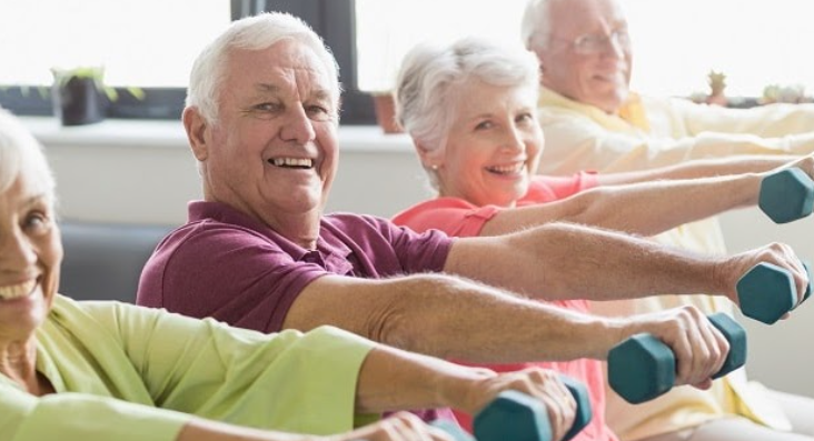 Group of elderly people exercising with dumbbells in a bright room.