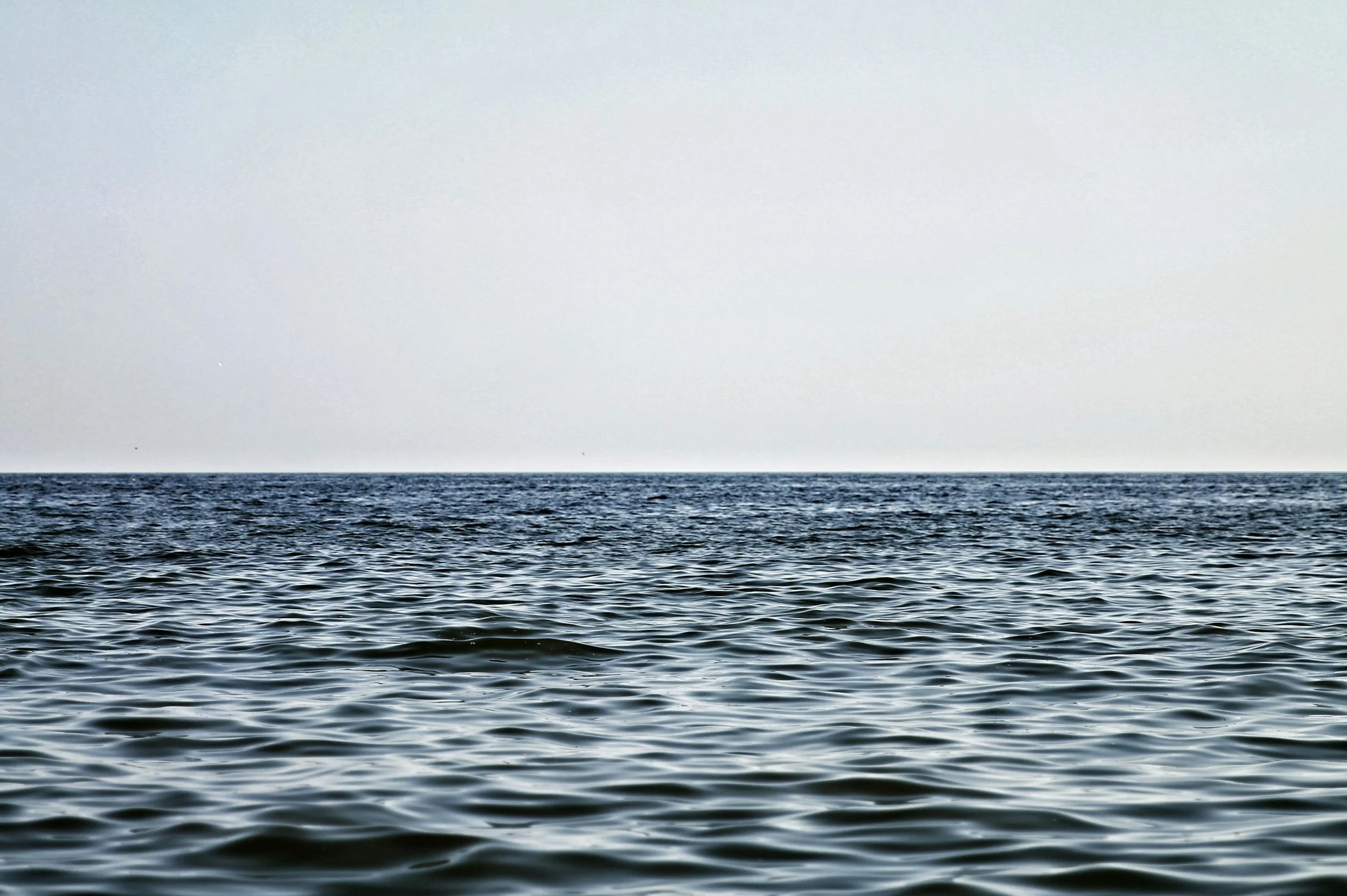 Calm ocean water with small waves, stretching to the horizon under a hazy sky.