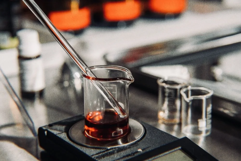 A laboratory beaker with a red liquid on a hot plate, with a glass pipette dripping the liquid into the beaker.