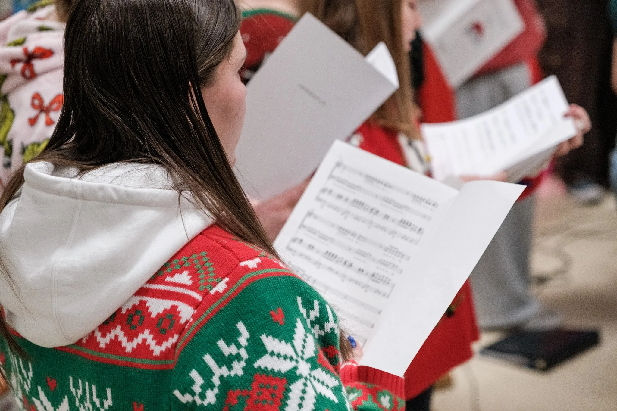 People wearing Christmas sweaters reading sheets of paper.