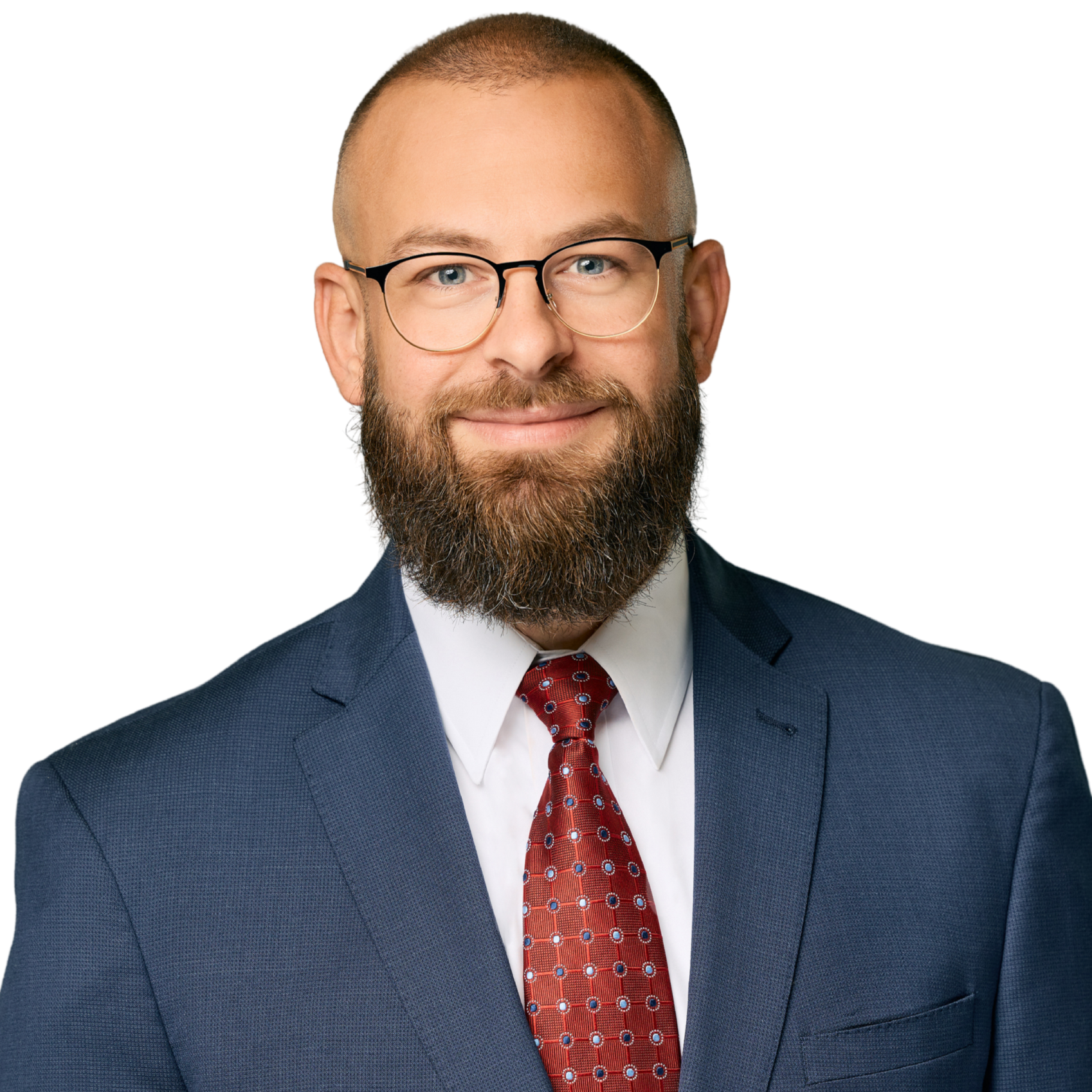 Portrait of a man with glasses and a beard, wearing a blue suit, white shirt, and red patterned tie, smiling.