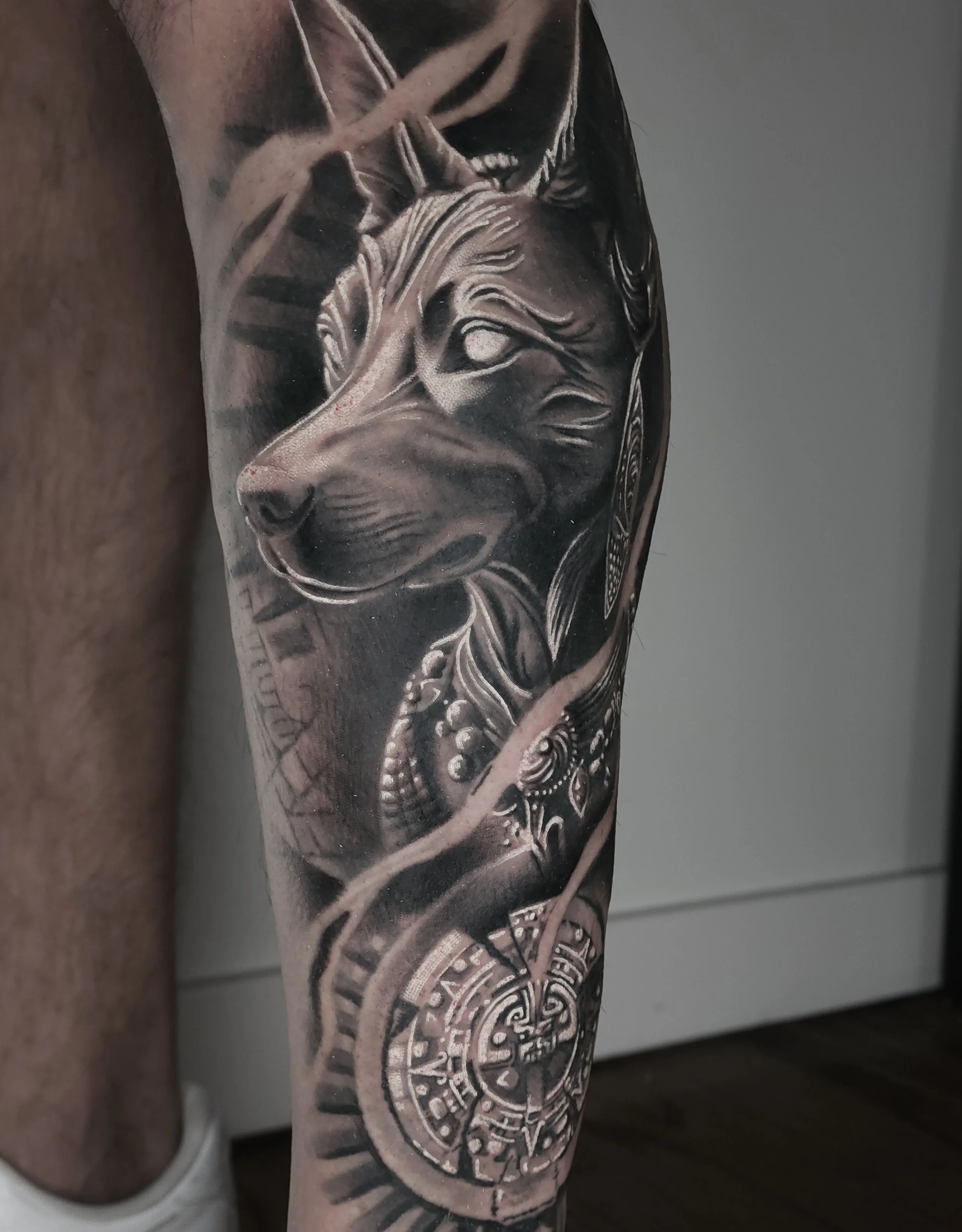Black and gray tattoo of a wolf's head with detailed fur, surrounded by abstract designs and a clock with Roman numerals on the person's arm.