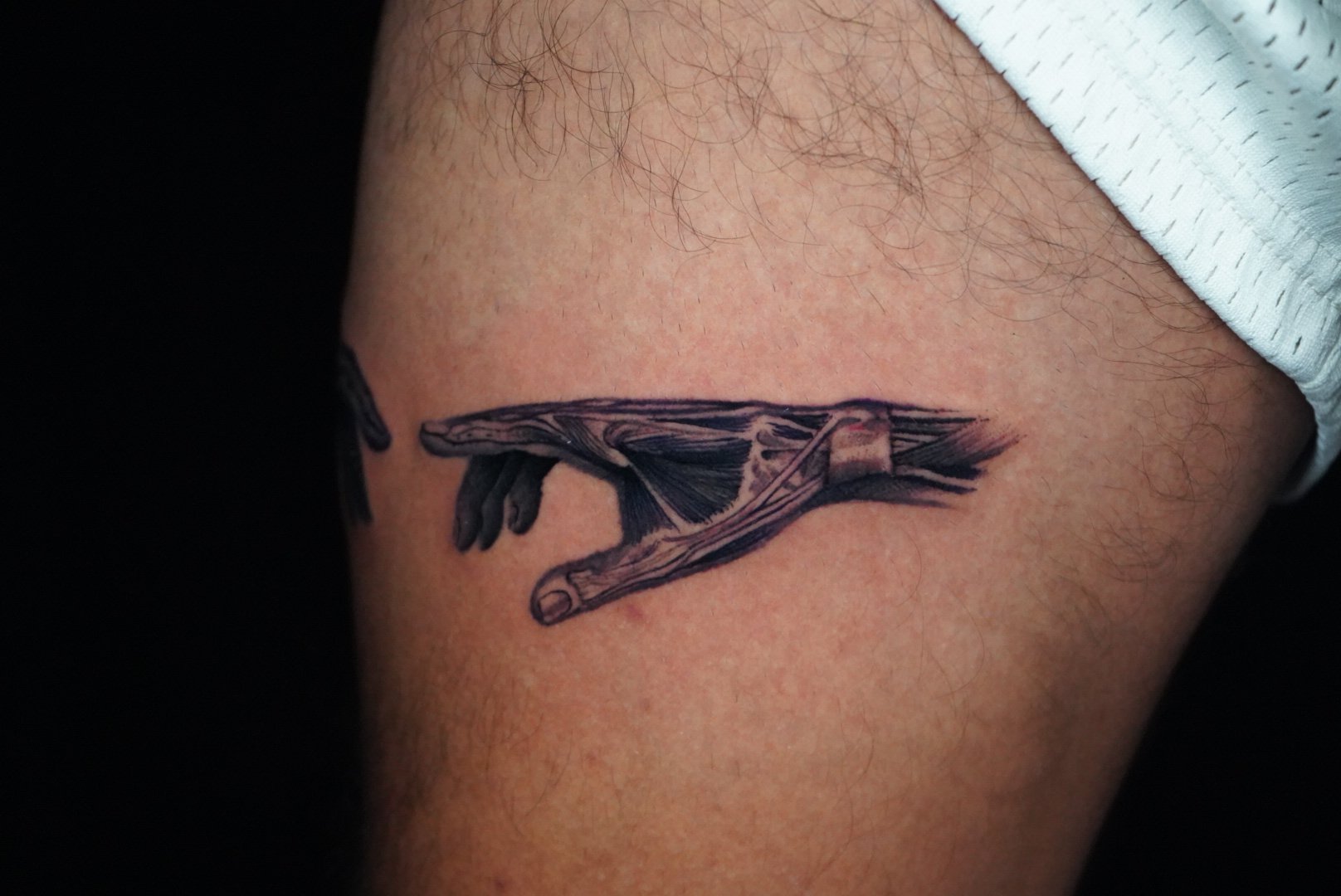 A tattoo of a human hand making a pinching gesture, inked with detailed shading, on a person's upper arm.