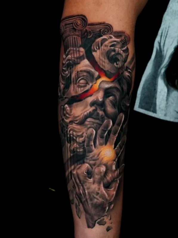 A detailed black and gray tattoo of a classical sculpture of a face, with a colorful tear running down, and a hand holding a glowing orb.