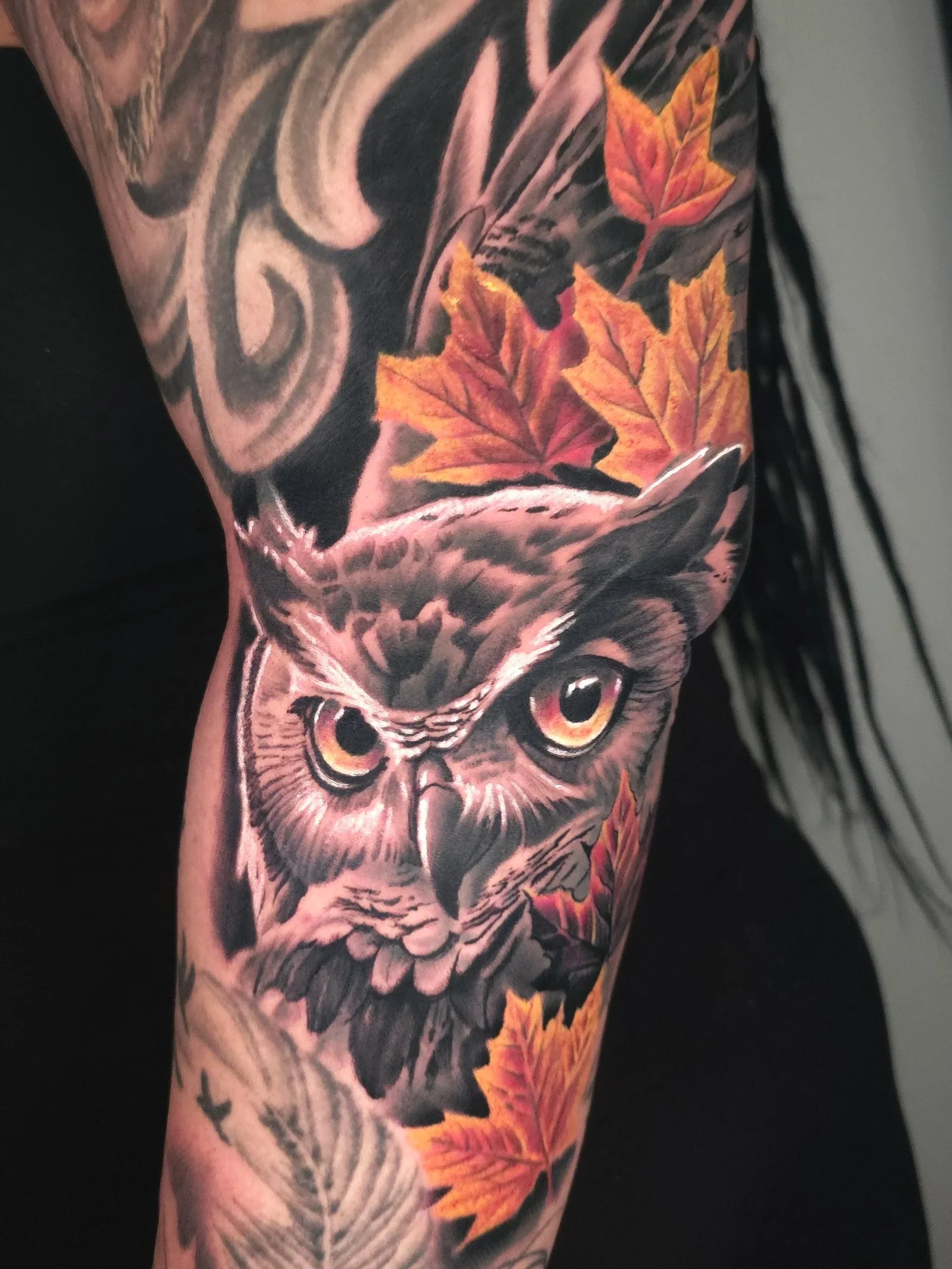 Tattoo of an owl surrounded by autumn leaves on a person's arm.