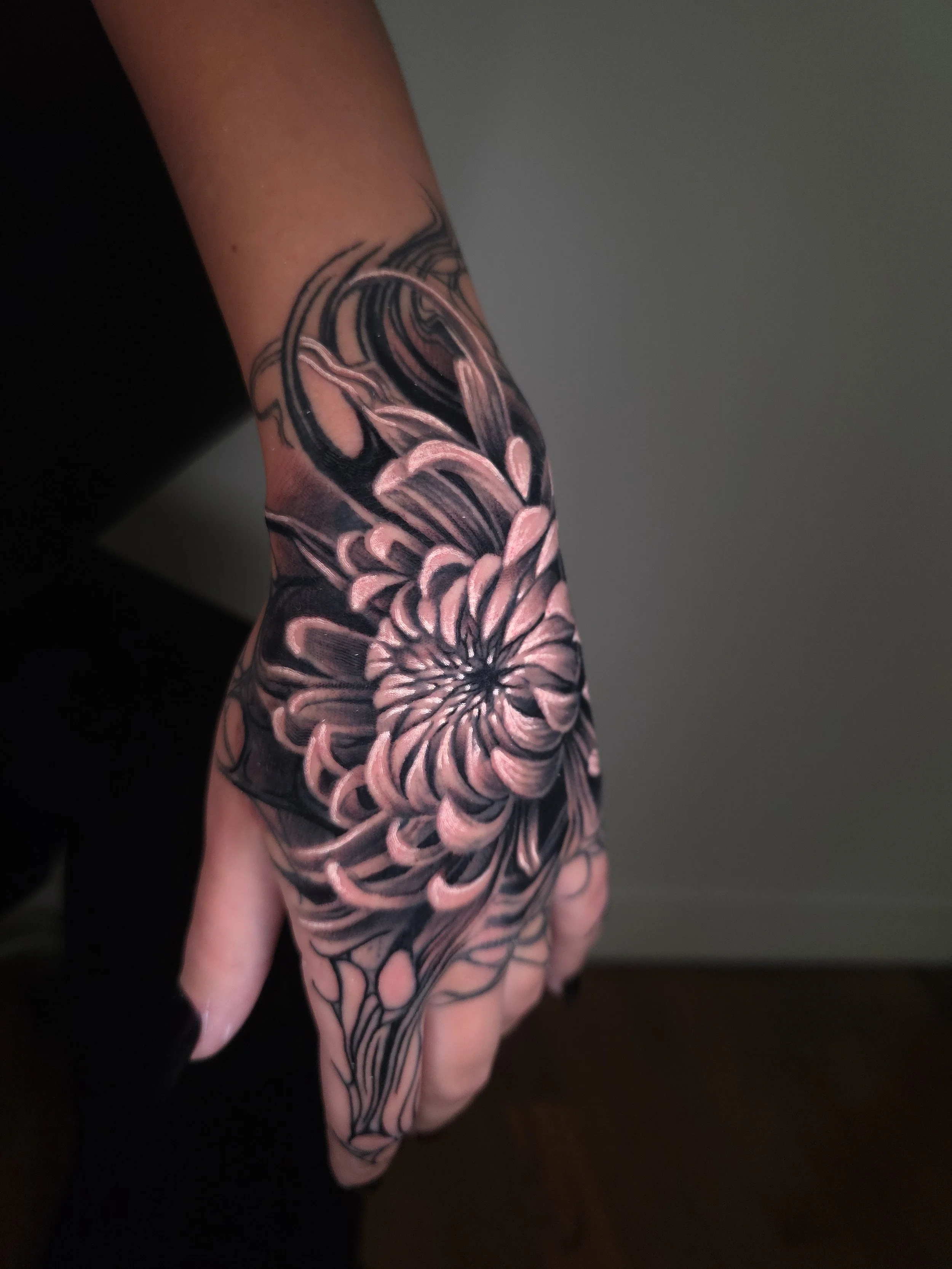 Close-up of a hand with a detailed, black and pink floral tattoo covering the back of the hand and wrist.