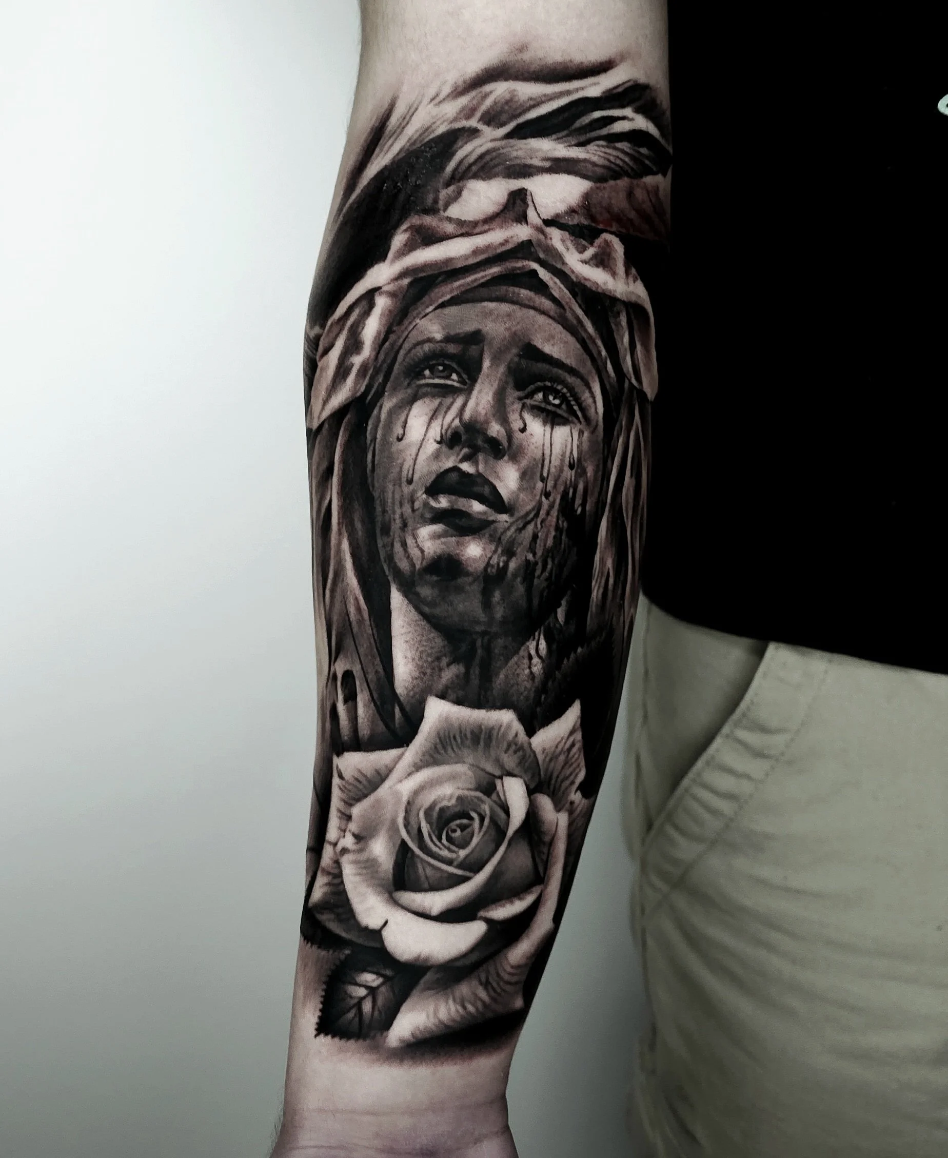 Tattoo of a woman's face with tears and a rose on the arm.