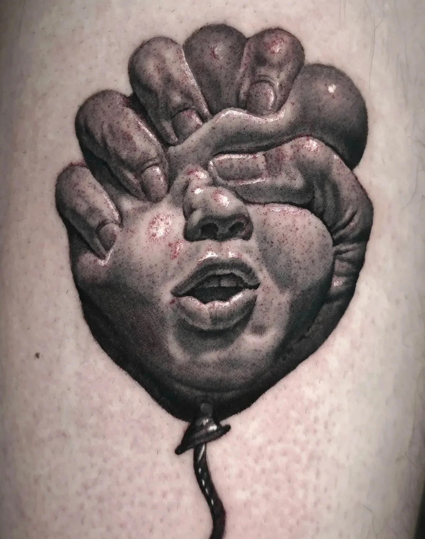 Tattoo of a balloon with a child's face, featuring hands covering the eyes, on a person's skin.