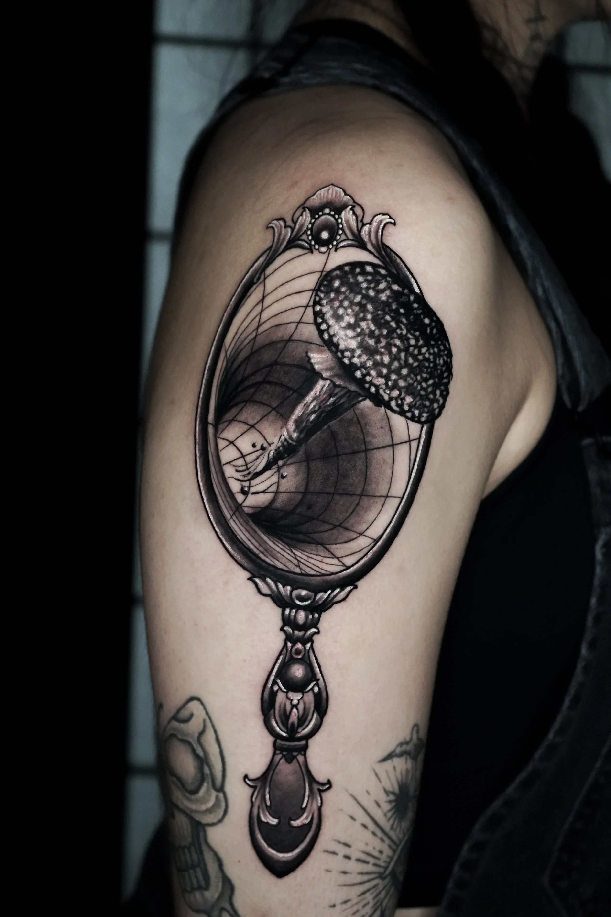 Tattoo of a mushroom inside an ornate mirror frame on a person's upper arm.