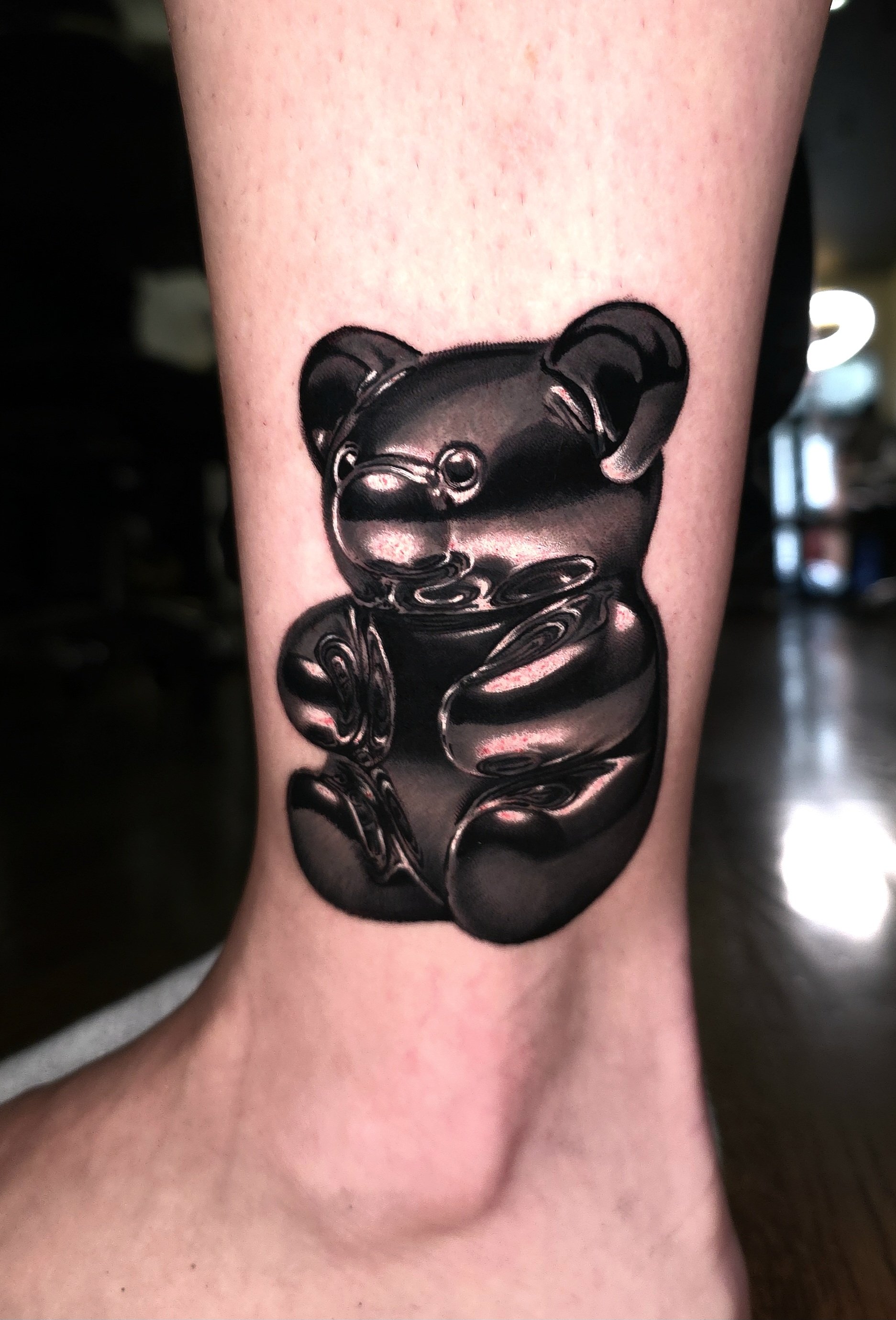 A tattoo of a reflective, shiny black teddy bear on a person's lower leg.