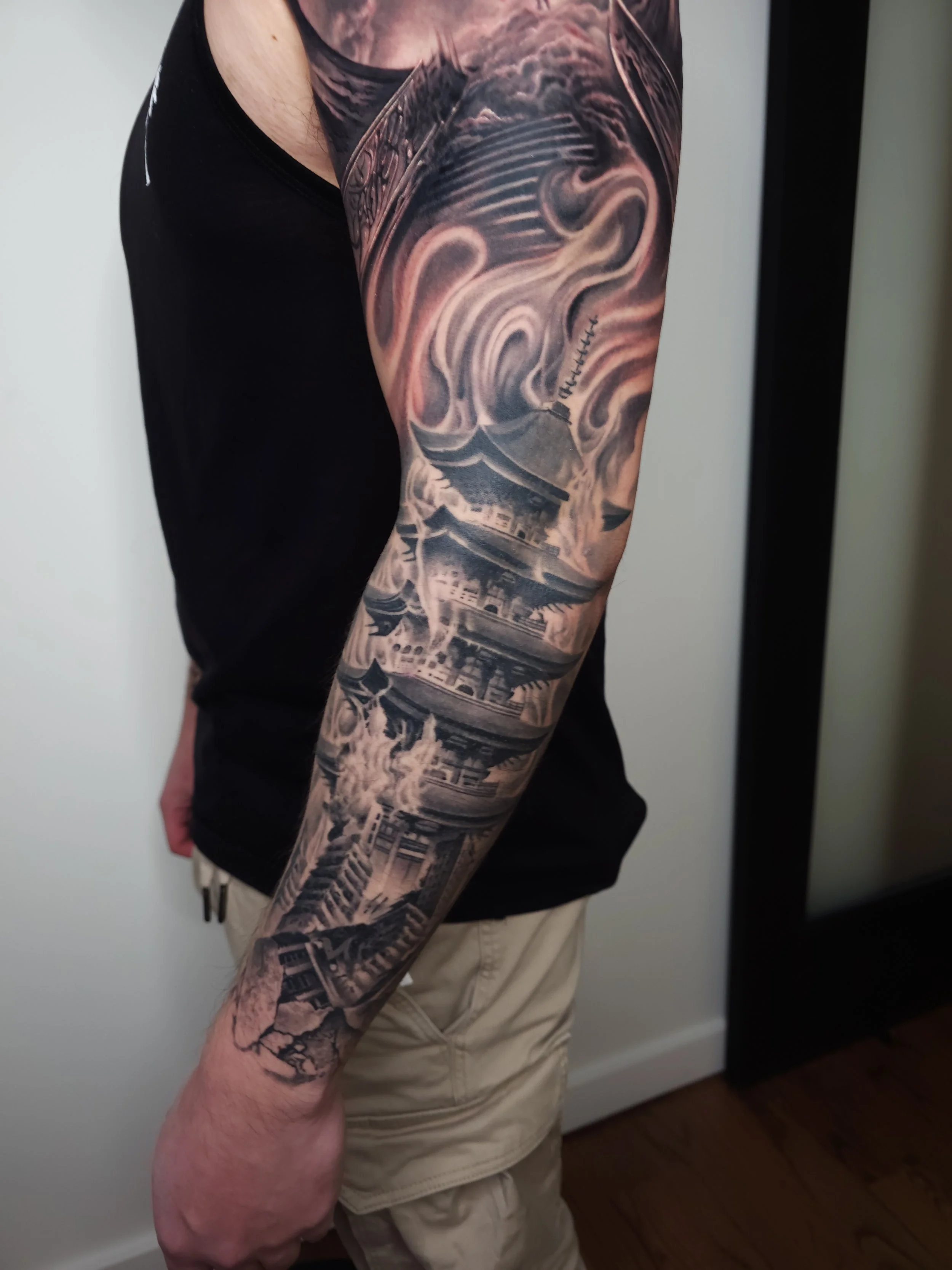 Tattoo of a traditional Japanese pagoda with swirling smoke or clouds surrounding it on a person's arm.