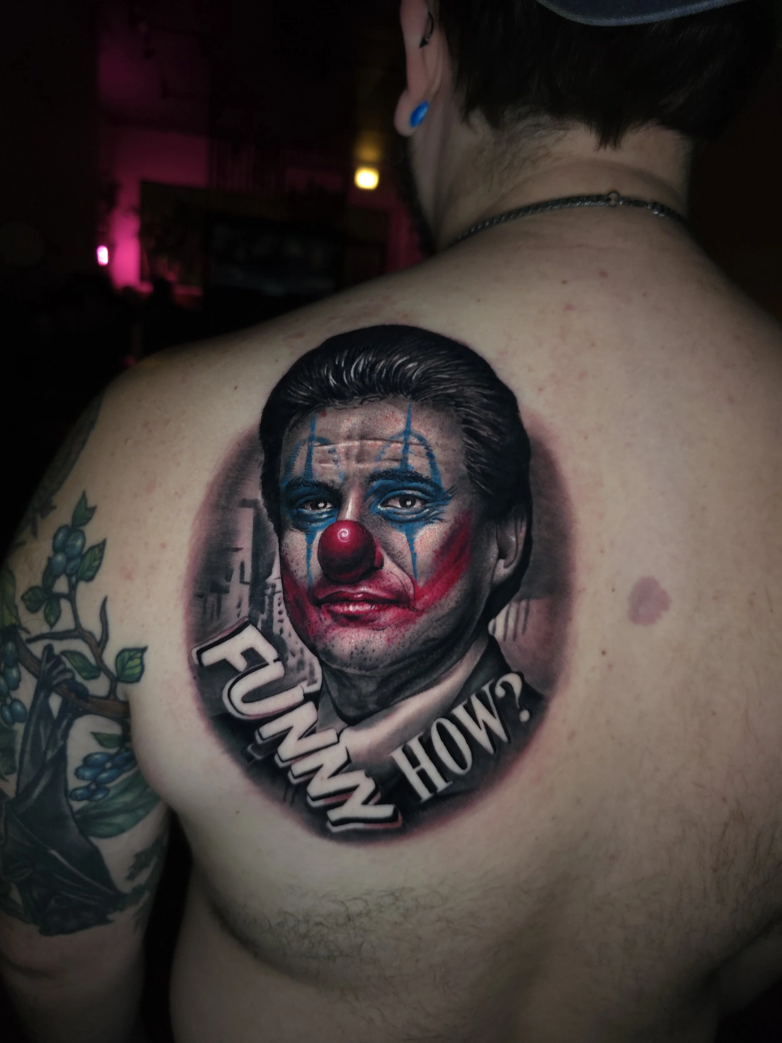 Tattoo of a man's face with clown makeup on a person's chest, with the words "How Funny" underneath.
