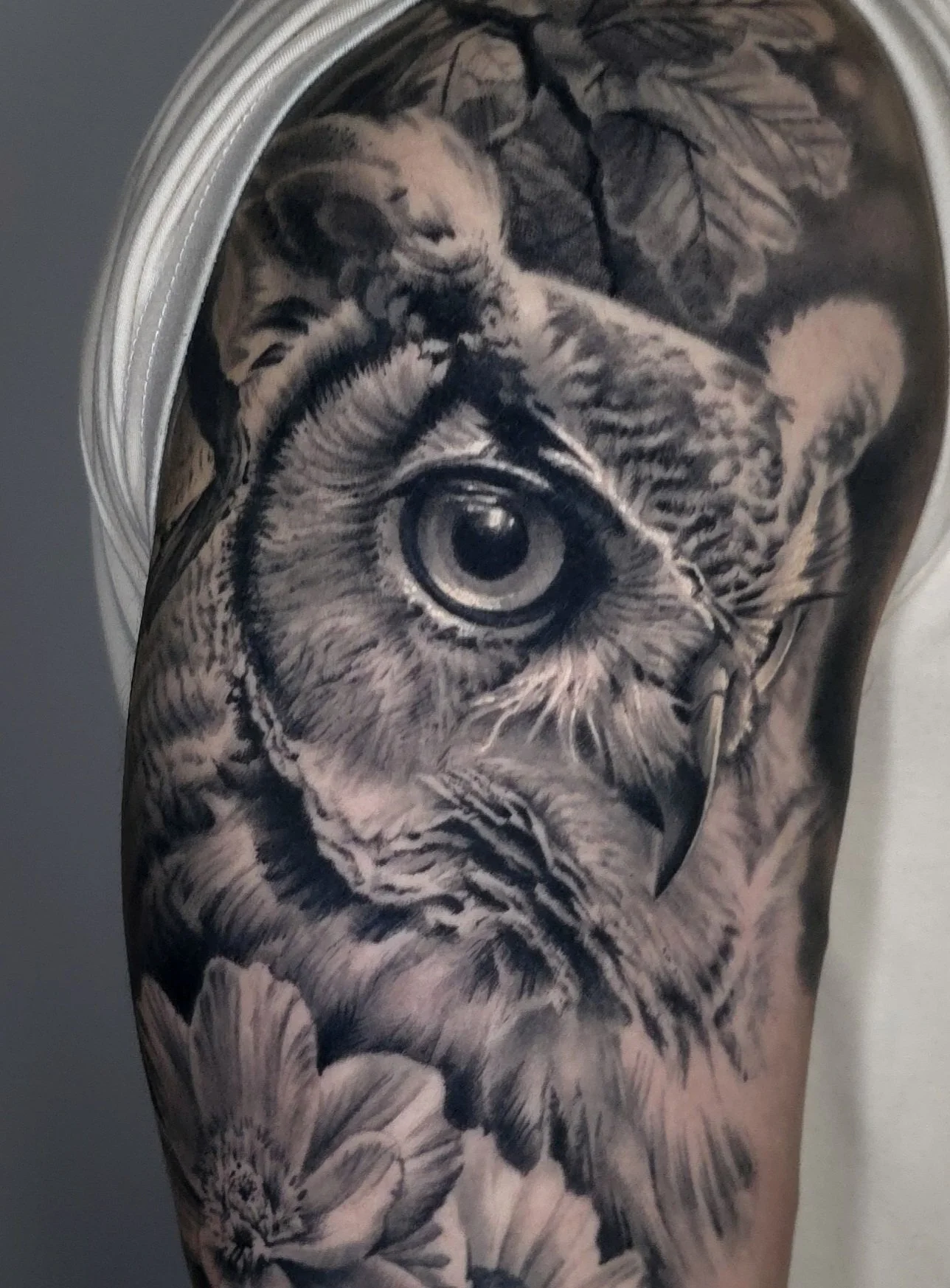 Black and gray tattoo of a tiger with detailed fur, eye, and facial features on a person's arm, surrounded by floral elements.