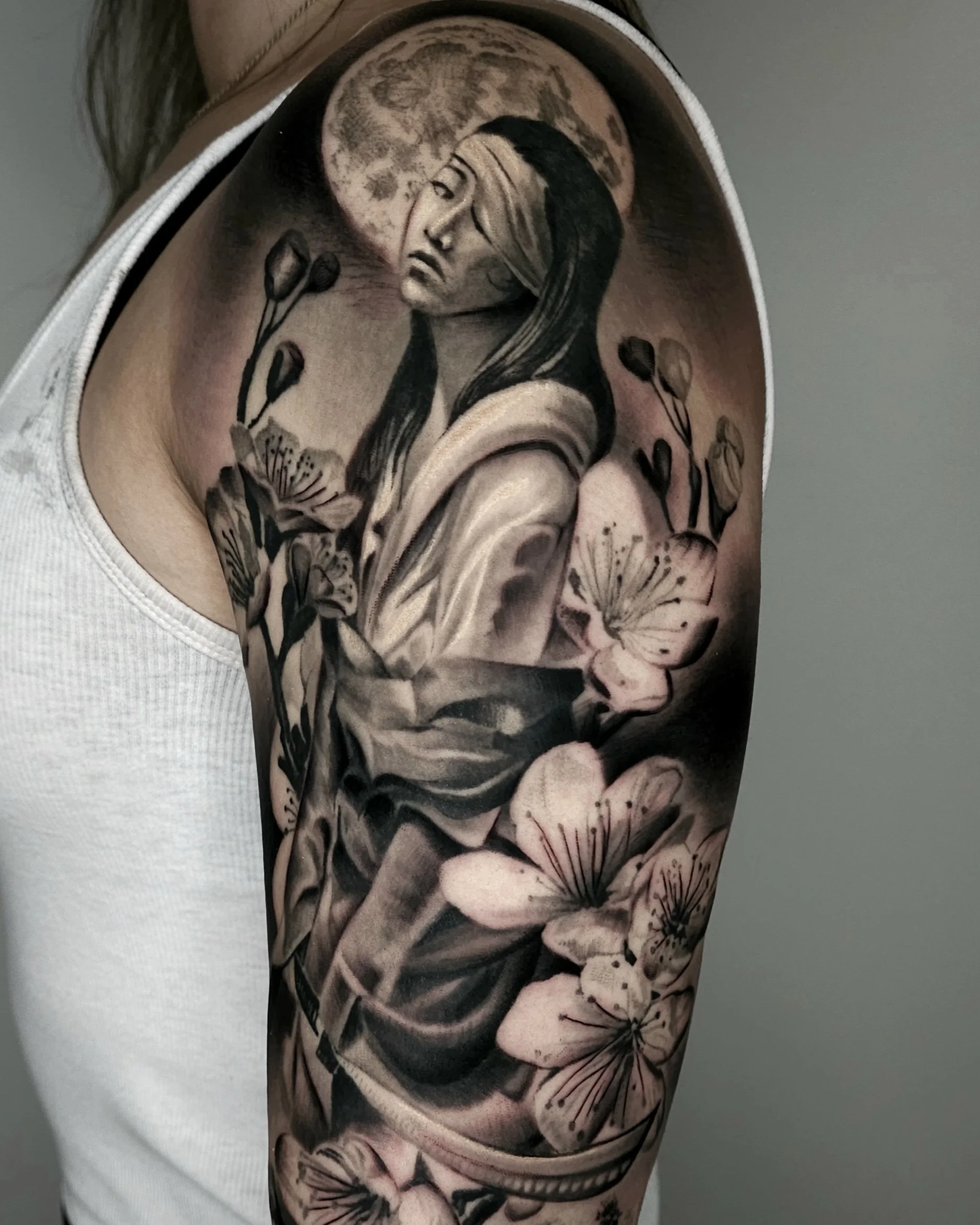 Black and gray floral tattoo on upper arm featuring a woman with long hair and a moon in the background.