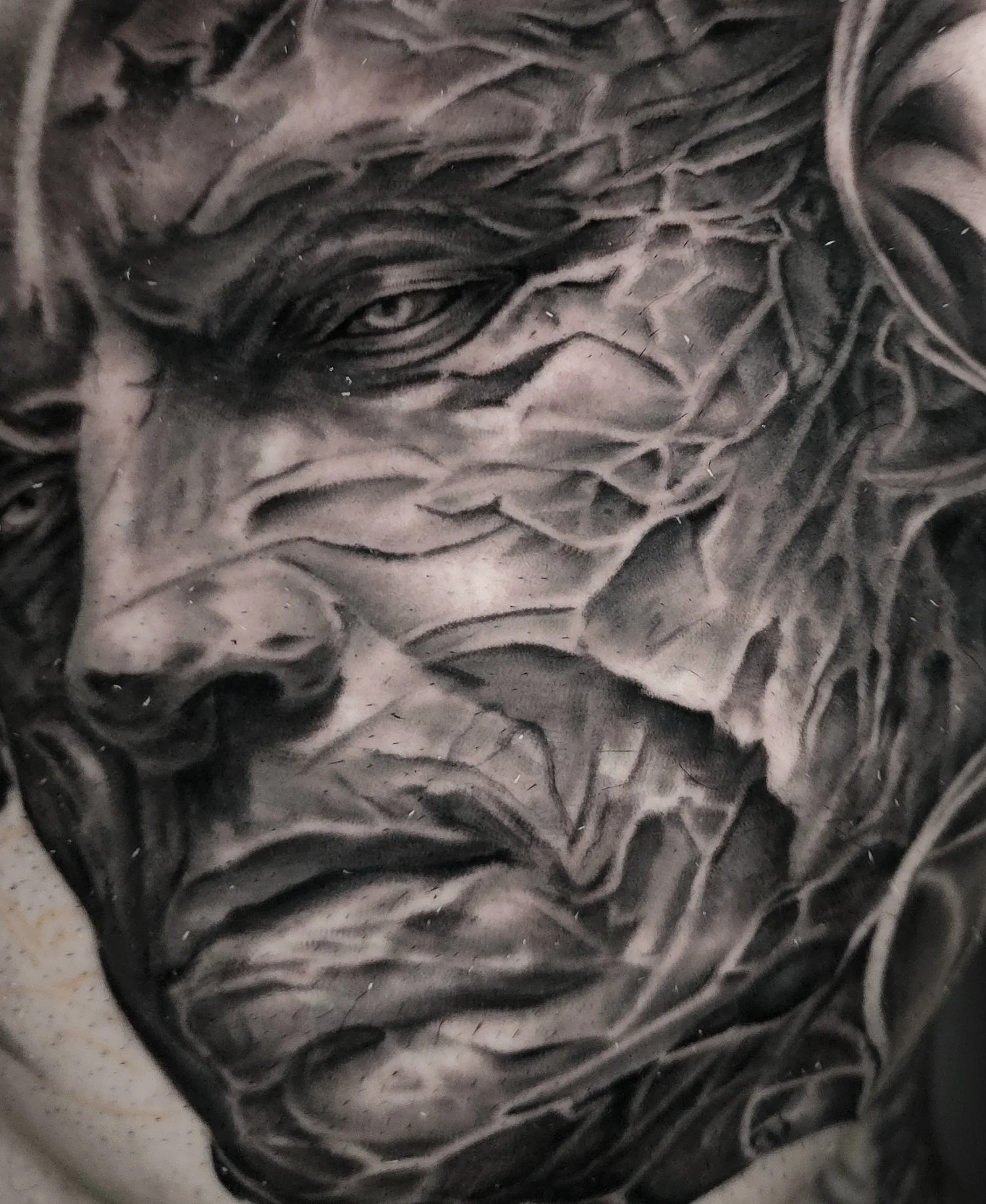 Close-up of a monochrome tattoo of a realistic human face, showing detailed features and shading.