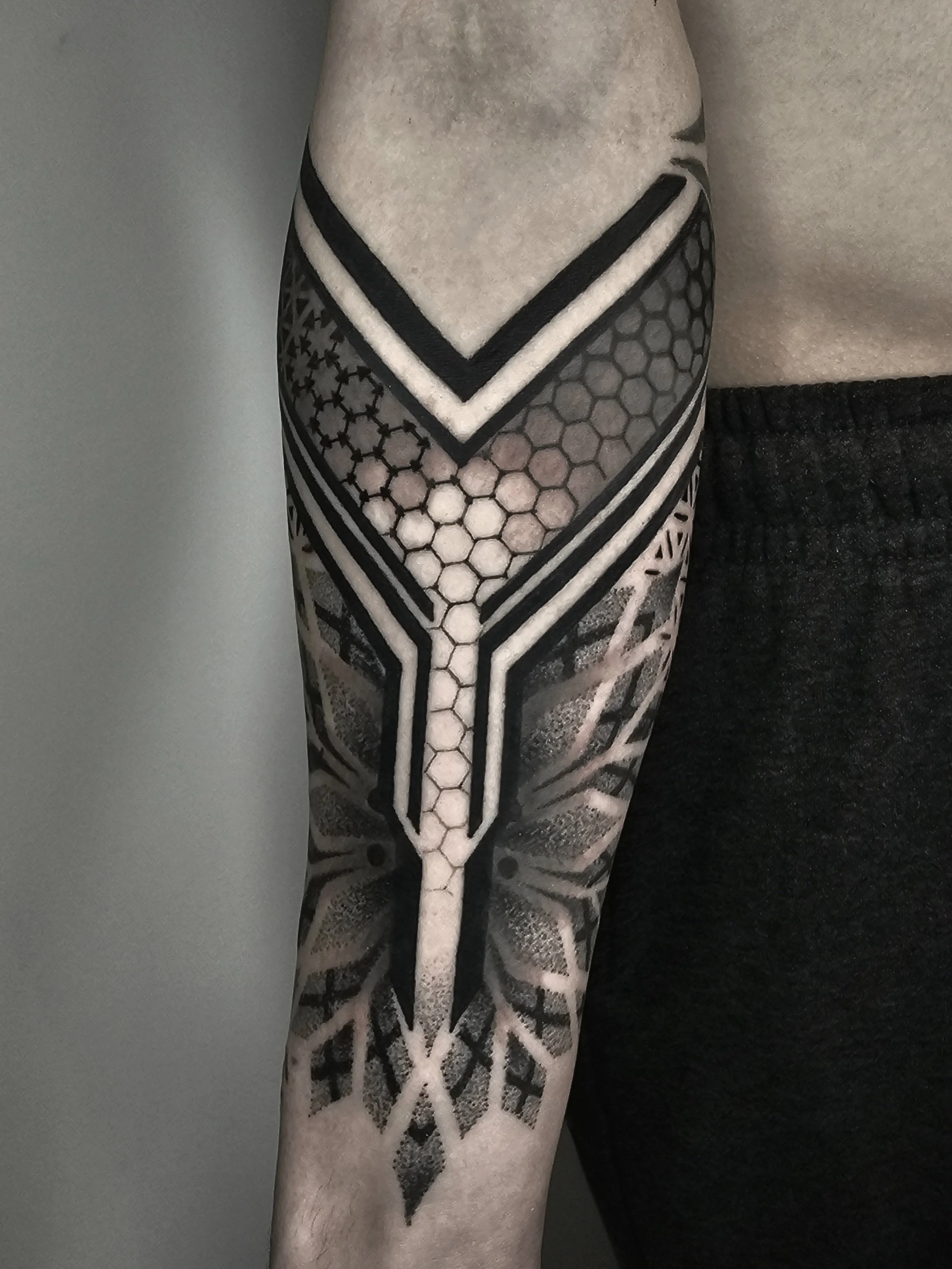 Black and gray geometric tattoo on a person's upper arm and shoulder, featuring honeycomb patterns, hexagons, and abstract shapes.