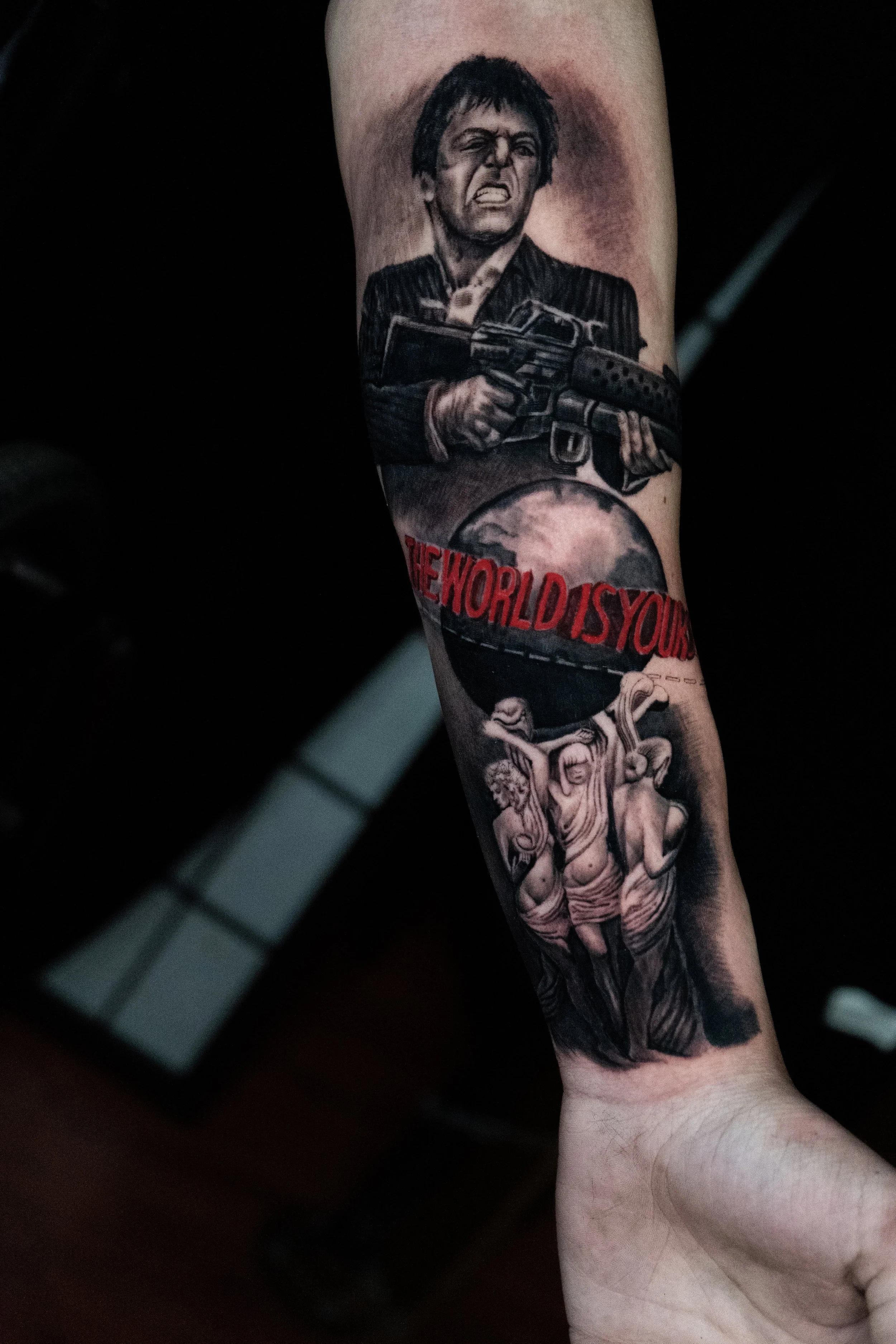 Tattoo of a woman holding a gun, a globe with the text "THE WORLD IS YOURS," and Monalisa sculptures.