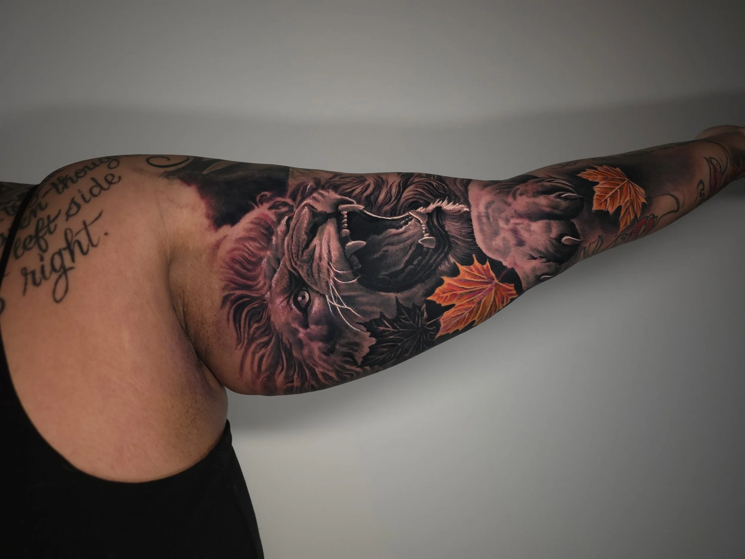 Tattoo of a lion's face with its mouth open, surrounded by autumn leaves on a person's arm.