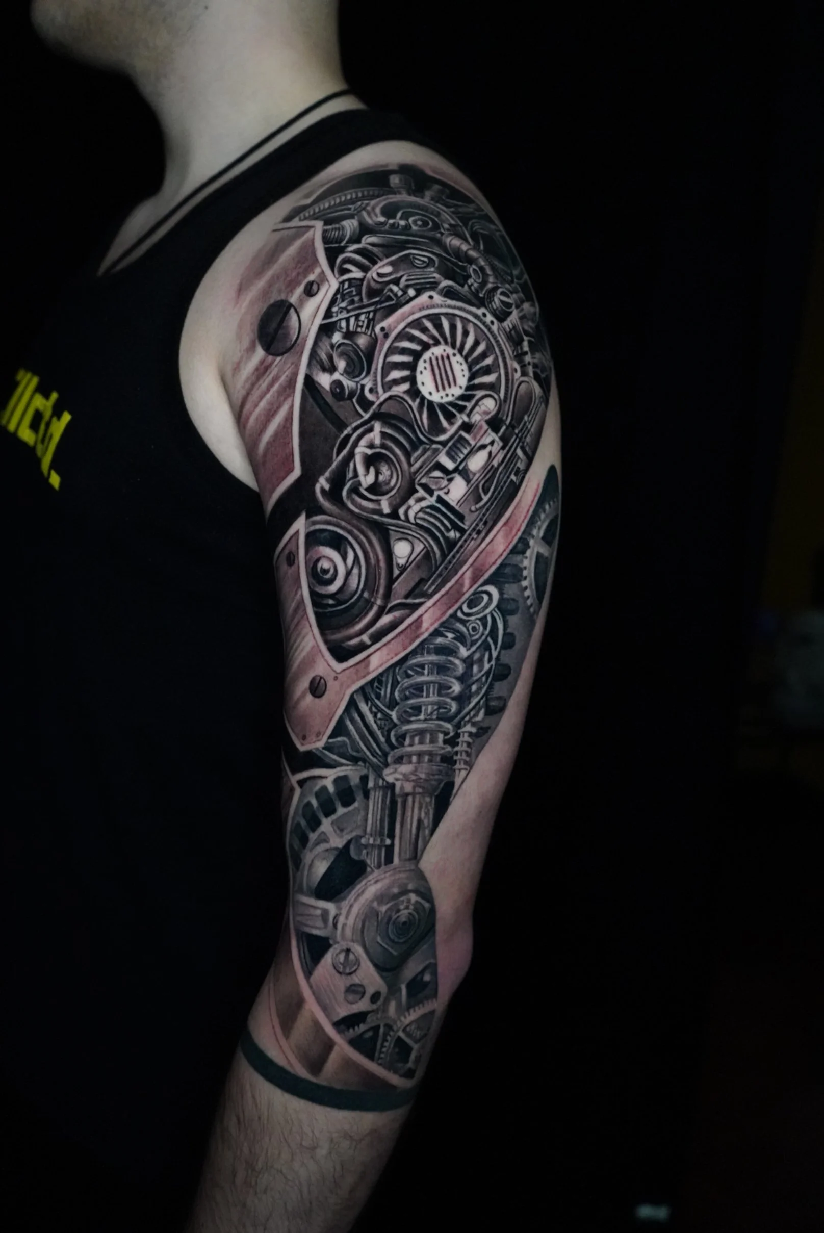 A detailed black and gray tattoo of mechanical gears and machinery on a person's upper arm and shoulder.
