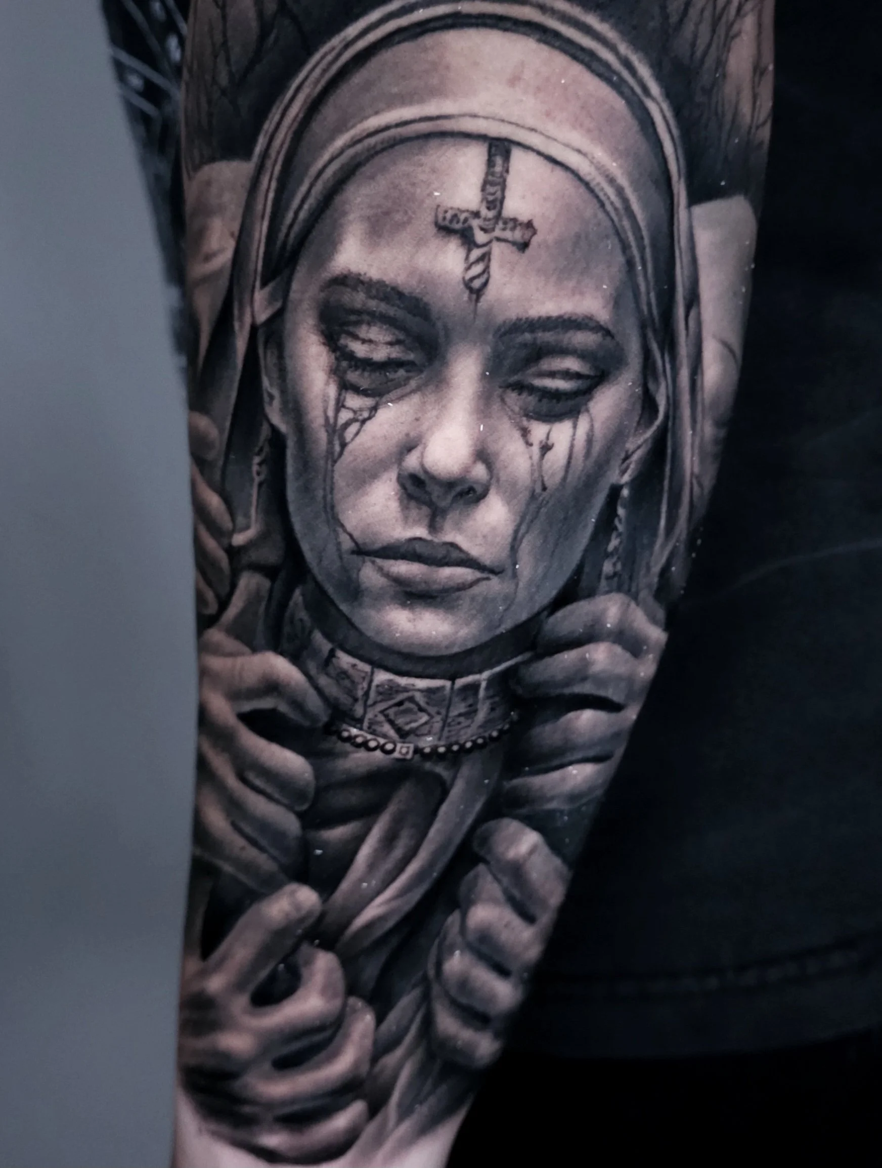 A detailed black and gray tattoo of a woman with tears on her cheeks, wearing a headscarf and a choker, with her hands holding the scarf or cloth around her neck.