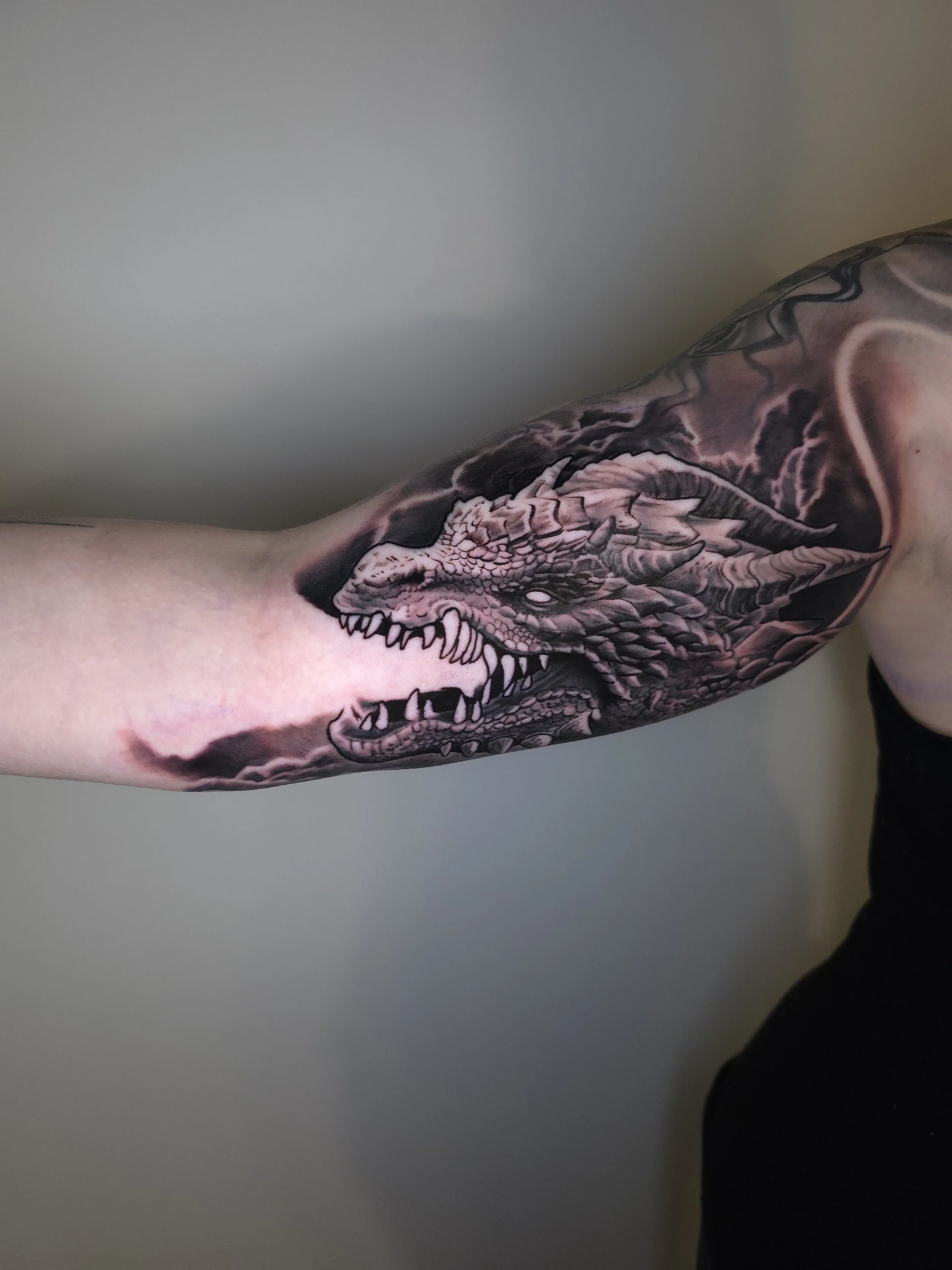 Tattoo of a dragon's head with open mouth, visible on a person's upper arm.