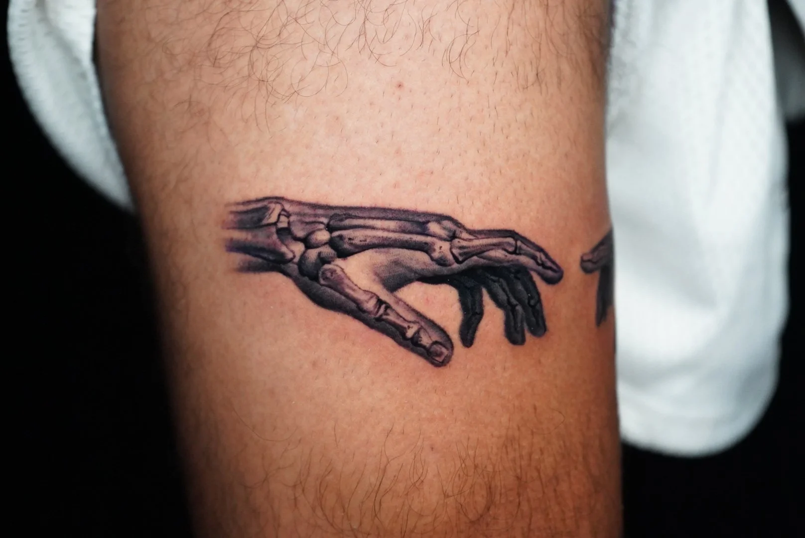 Tattoo of a realistic black and gray detailed hand in a reaching gesture on someone's upper arm.