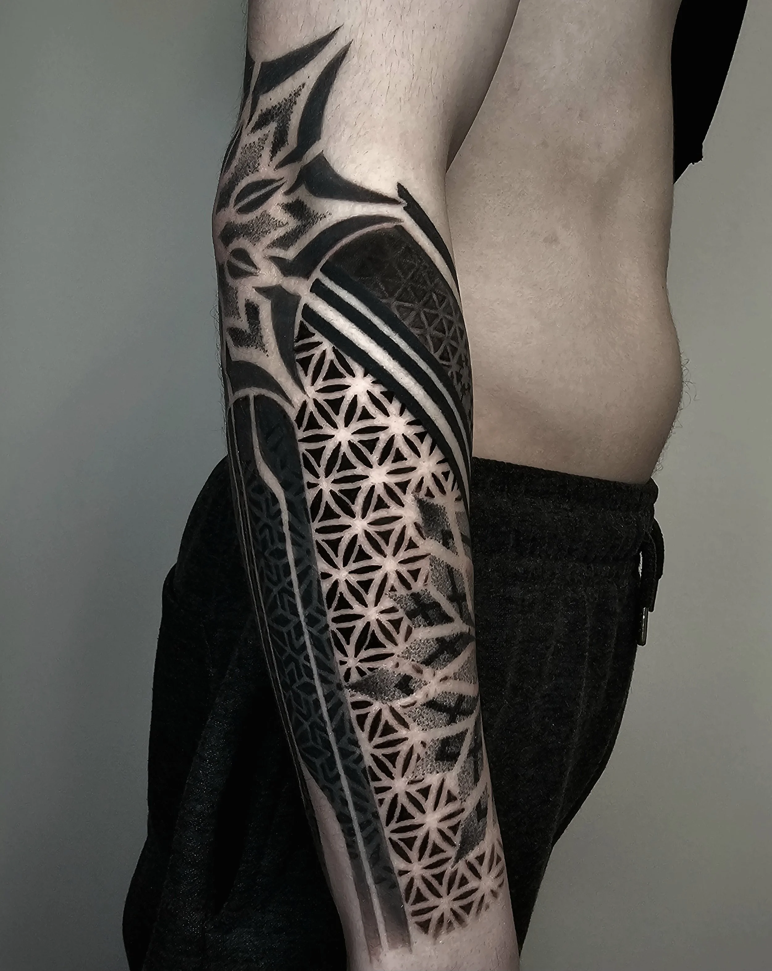 A person's arm with a detailed black and grey geometric and tribal tattoo.
