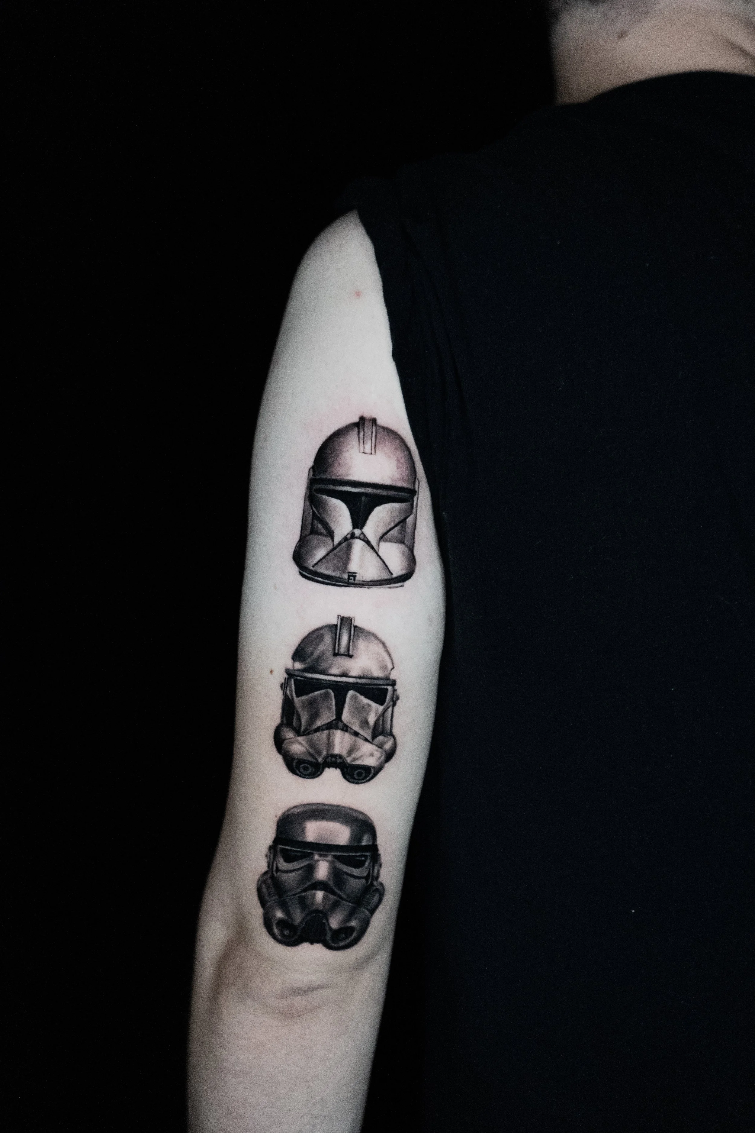 Tattoo of three different types of Stormtrooper helmets from Star Wars on person's upper arm.