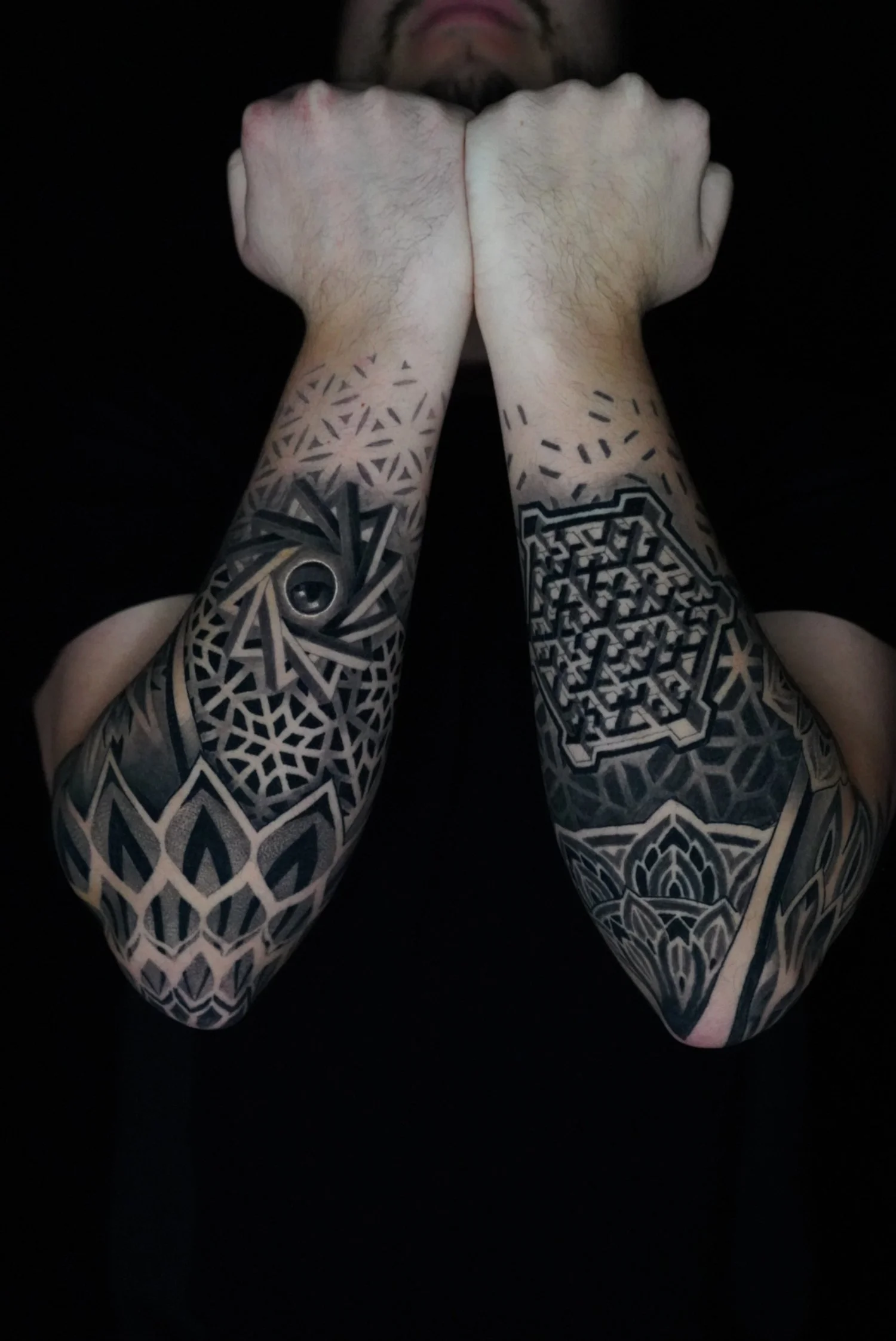 Close-up of a person's hands and forearms, with tattoos and crossed fists, against a dark background.