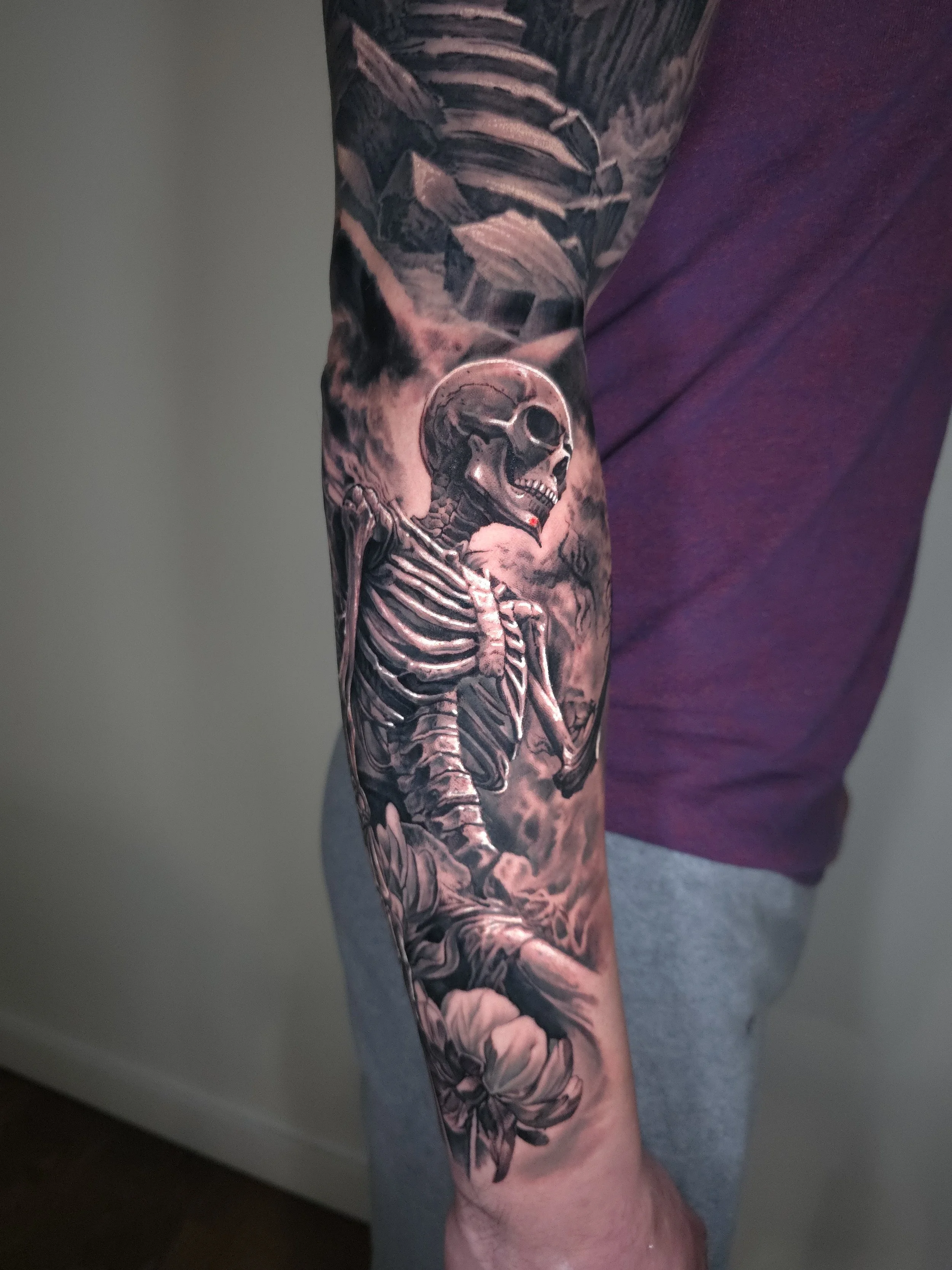 Detailed black and gray tattoo of a skeleton with a moon behind it, on a person's forearm.