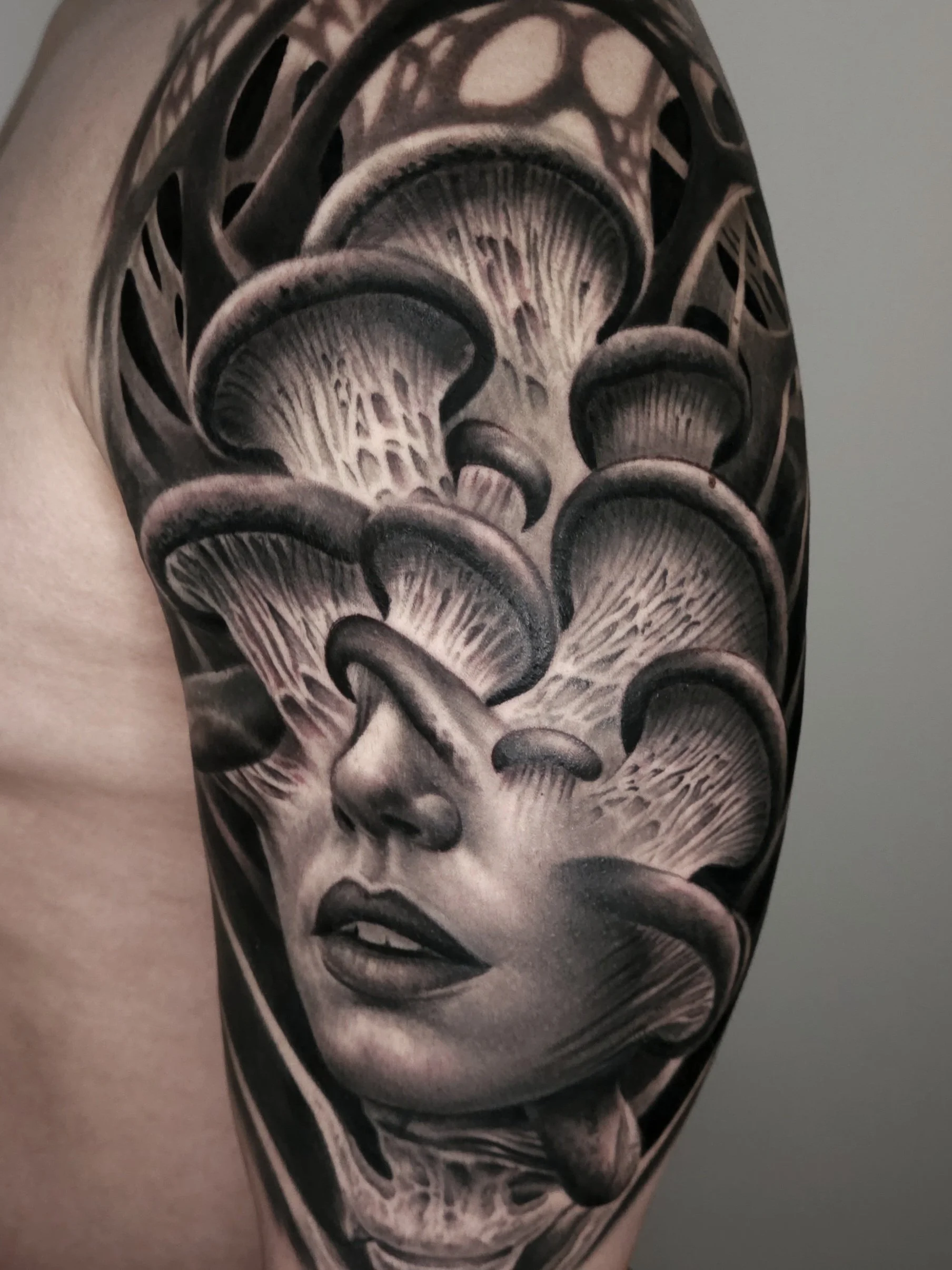 Black and gray tattoo of a woman's face with mushrooms growing around and over her head.
