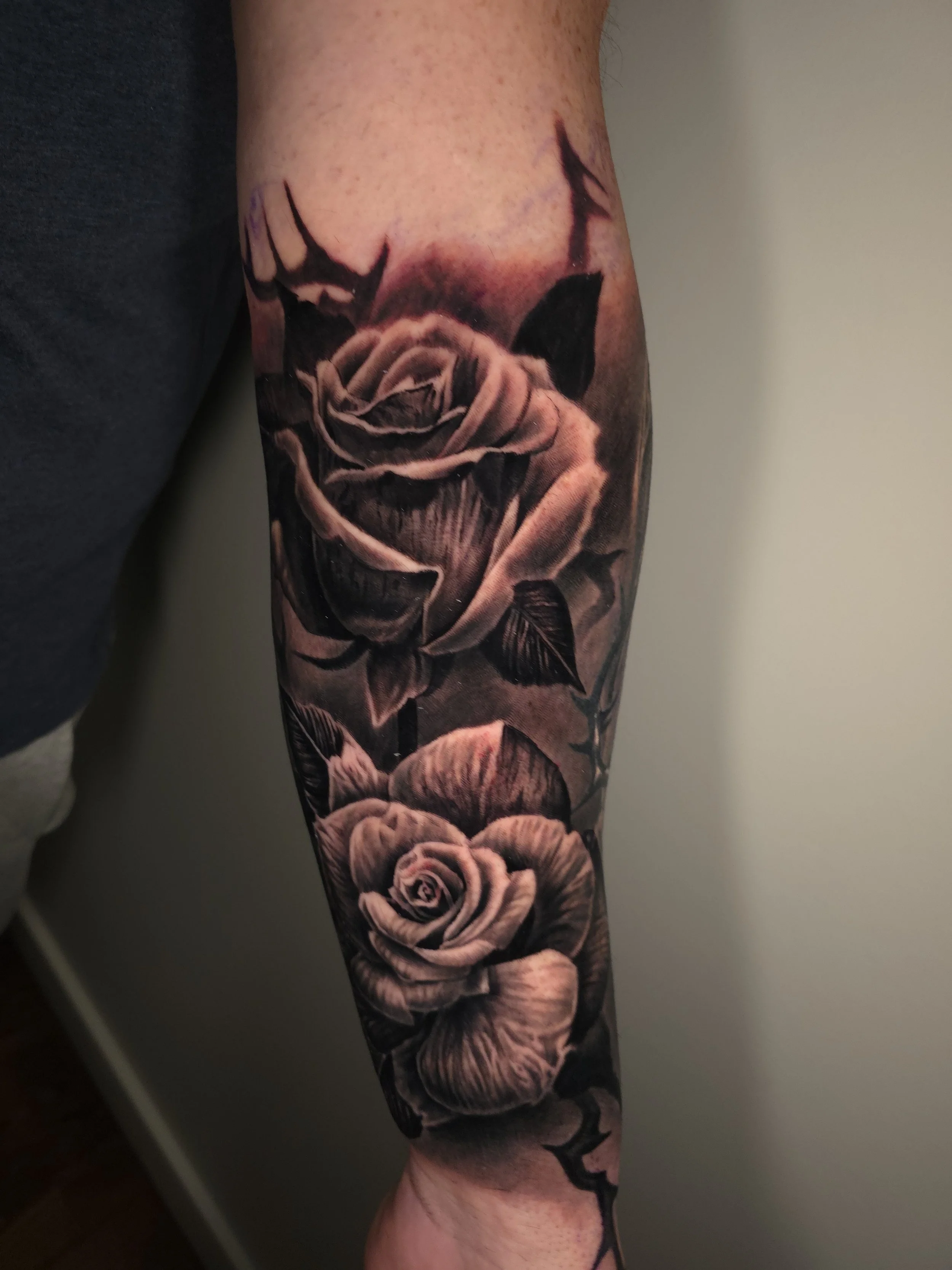Black and gray detailed tattoo of two roses on a person's arm.
