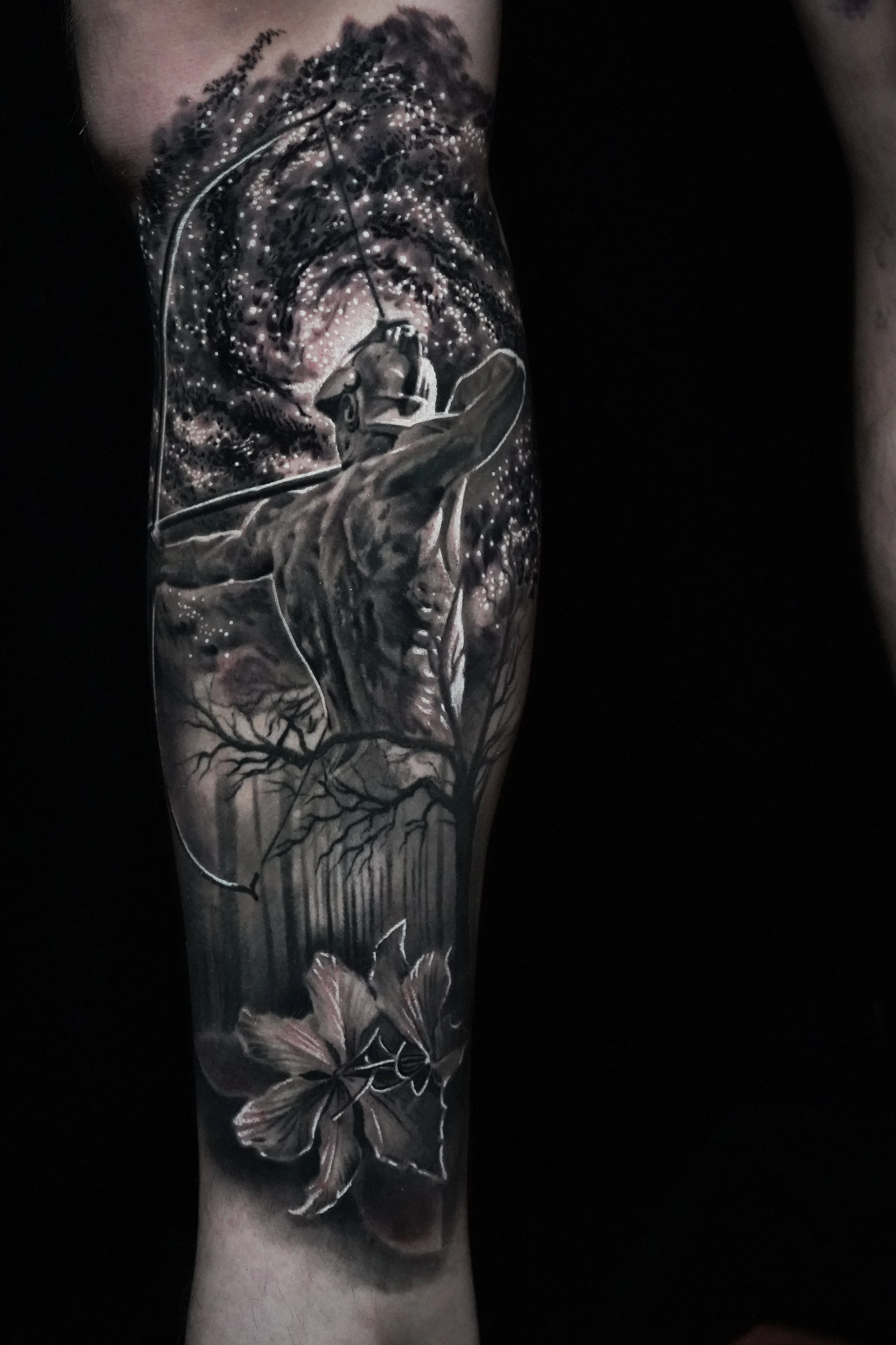 Black and gray tattoo of a helicopter flying above a forest with trees, a butterfly, and swirling starry sky.