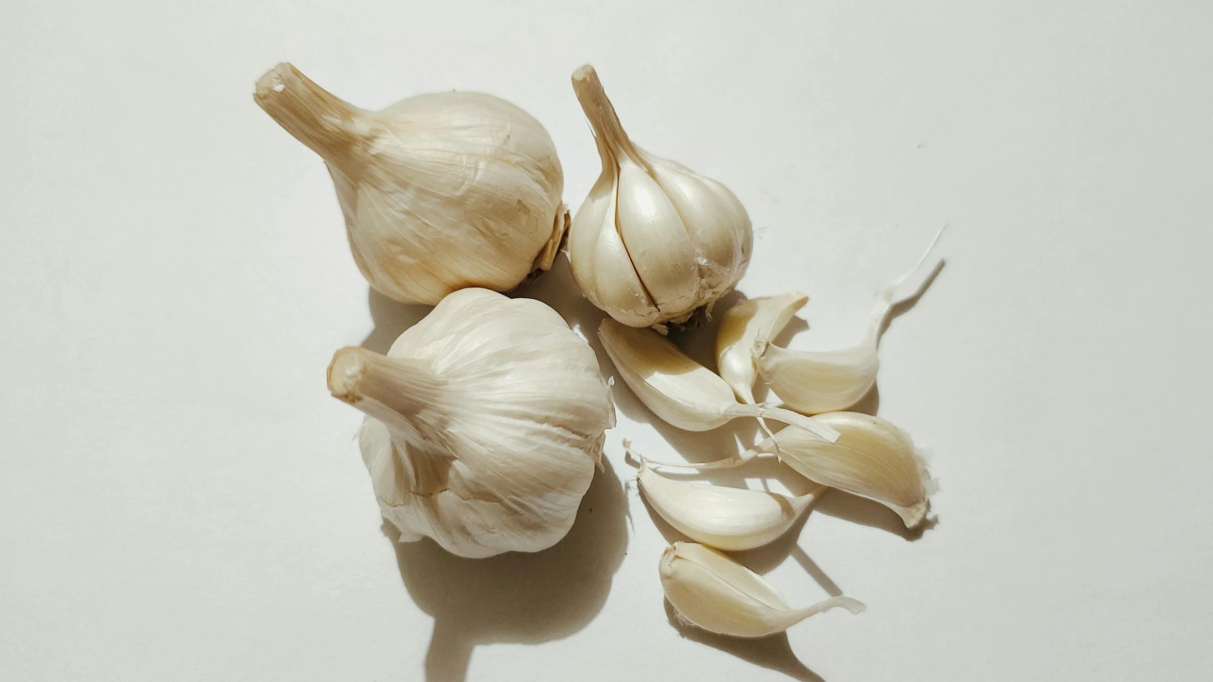 Three whole garlic bulbs and several garlic cloves on a white surface.