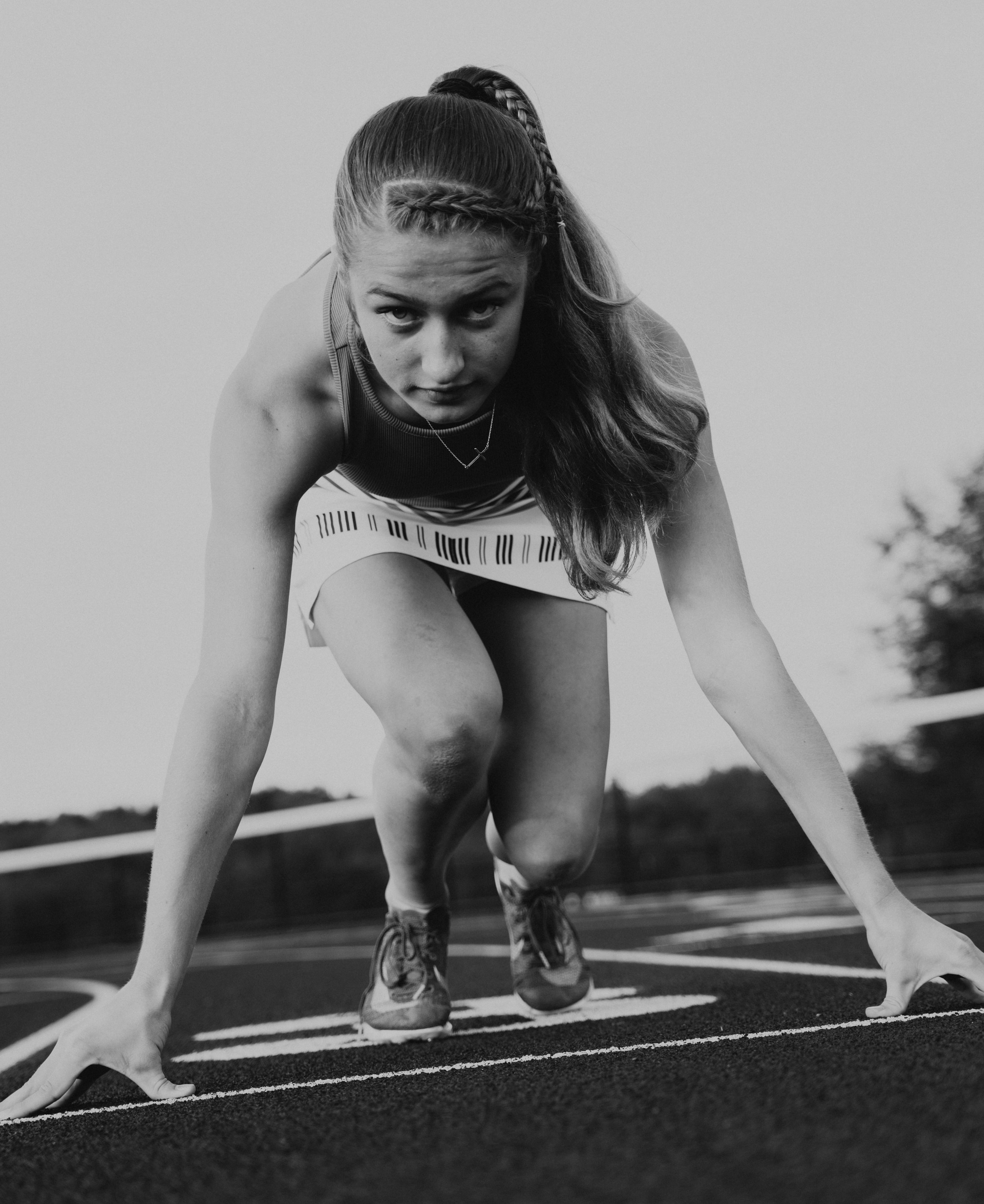 A young woman in athletic wear is in a sprinting position on a running track, preparing to start a race.