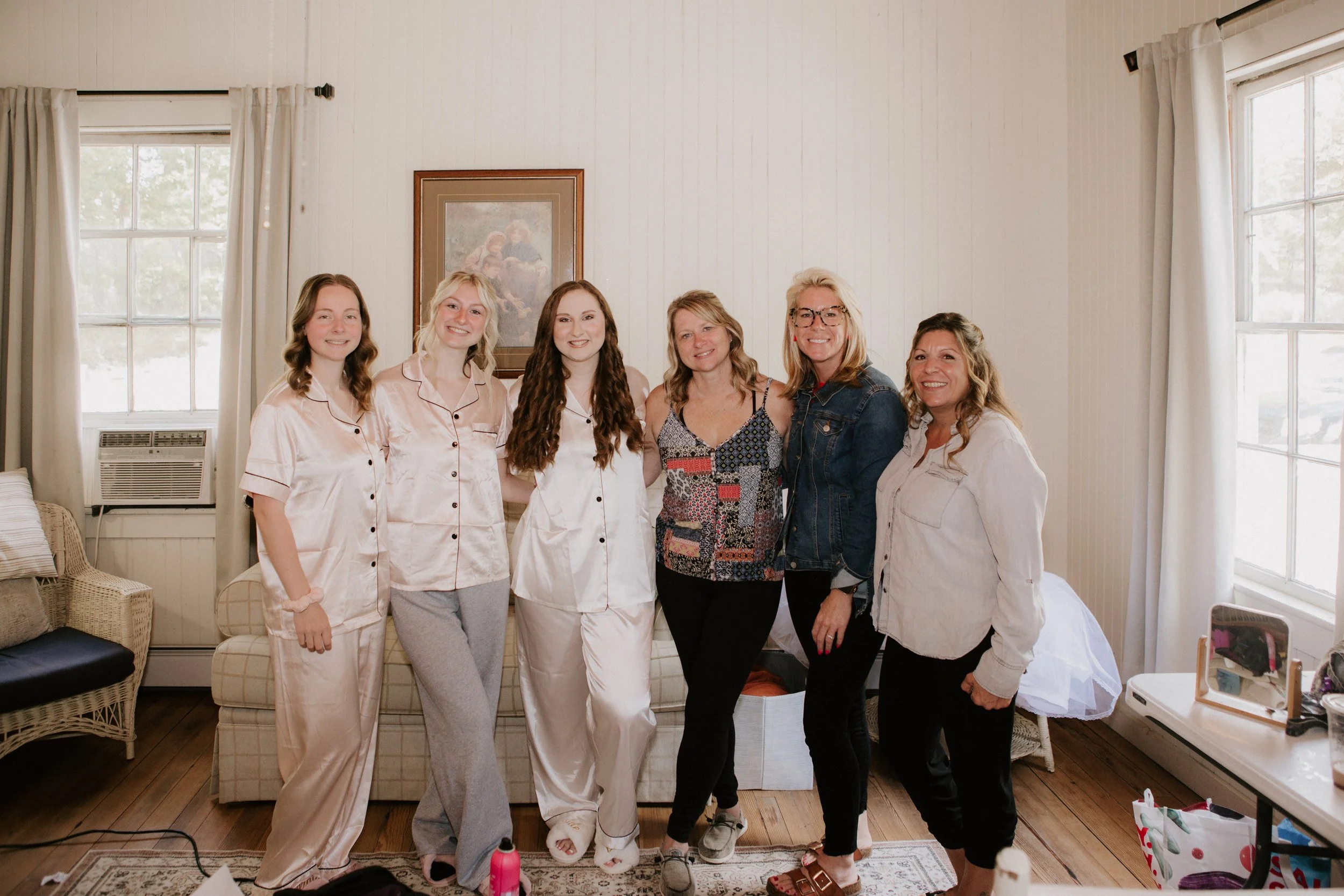 Group of six women standing together in a living room, some in pajamas, smiling at the camera.