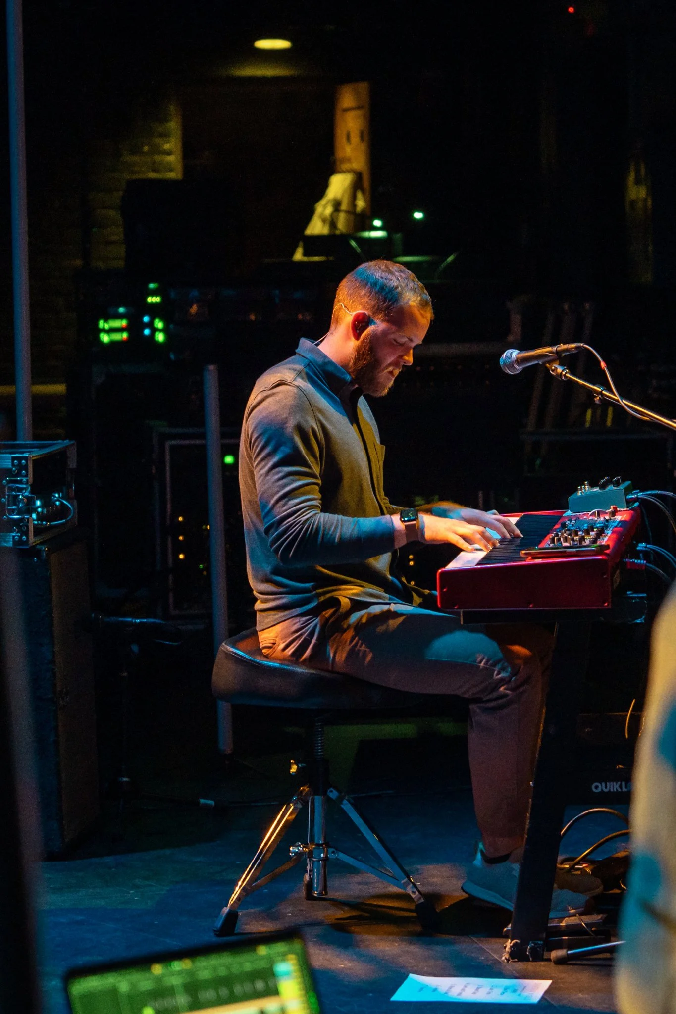 A man playing a red keyboard on a stage with dark background lights.