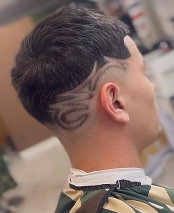 Side view of a young man's haircut featuring a geometric design shaved into the undercut on the side of his head.