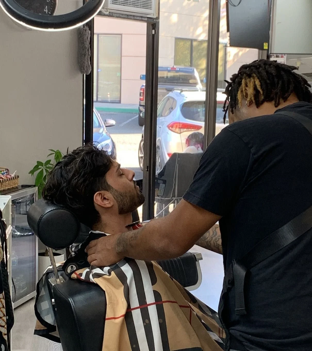 A man getting a haircut at a barbershop, with his eyes closed, while a barber stands close to him, grooming his beard.