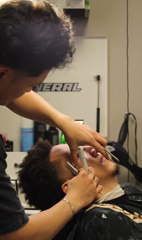 Barber shaping a customer's sideburn in a barbershop.