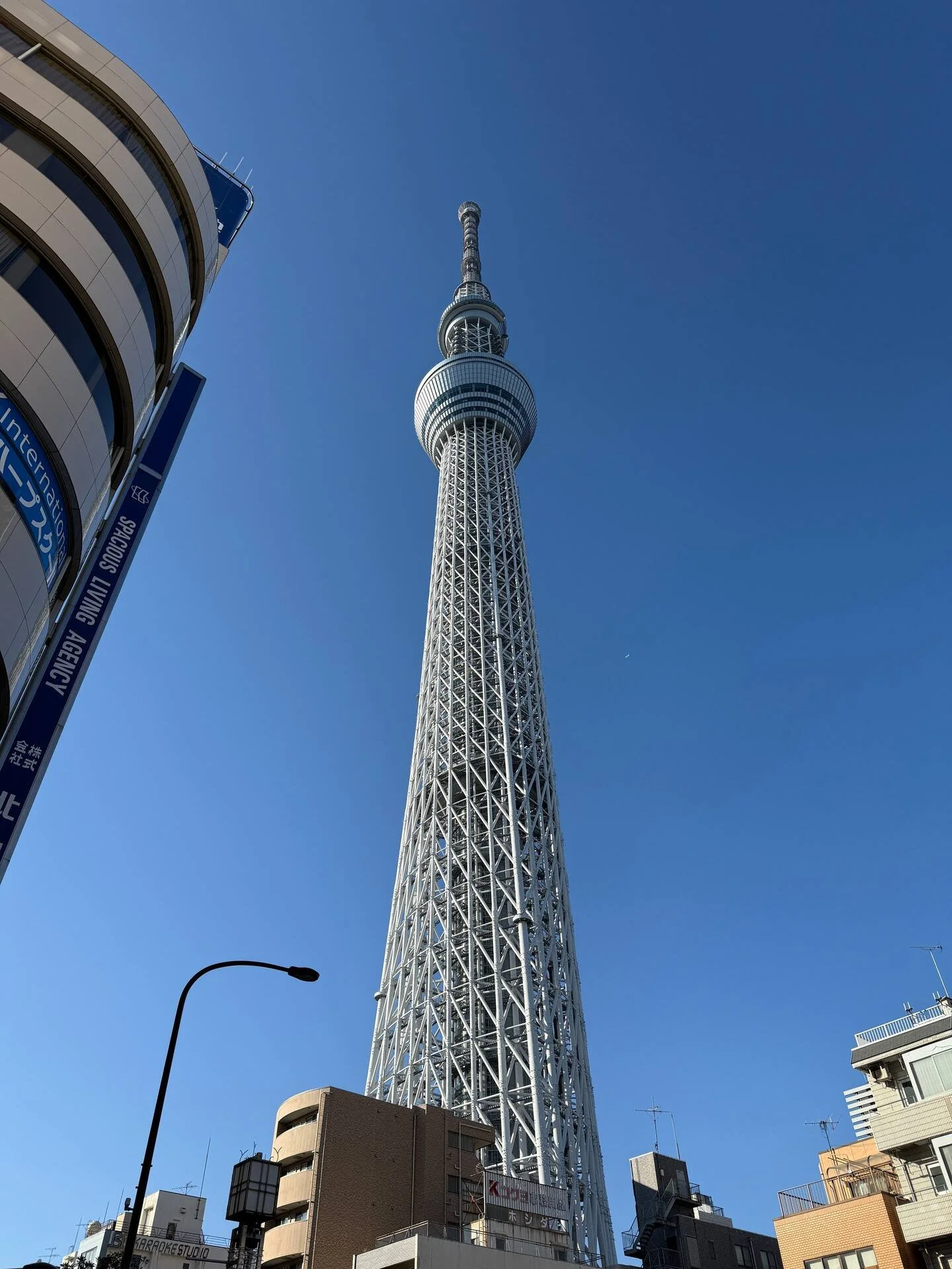 Tall observation tower against a clear blue sky, surrounded by buildings and streetlights in an urban area.
