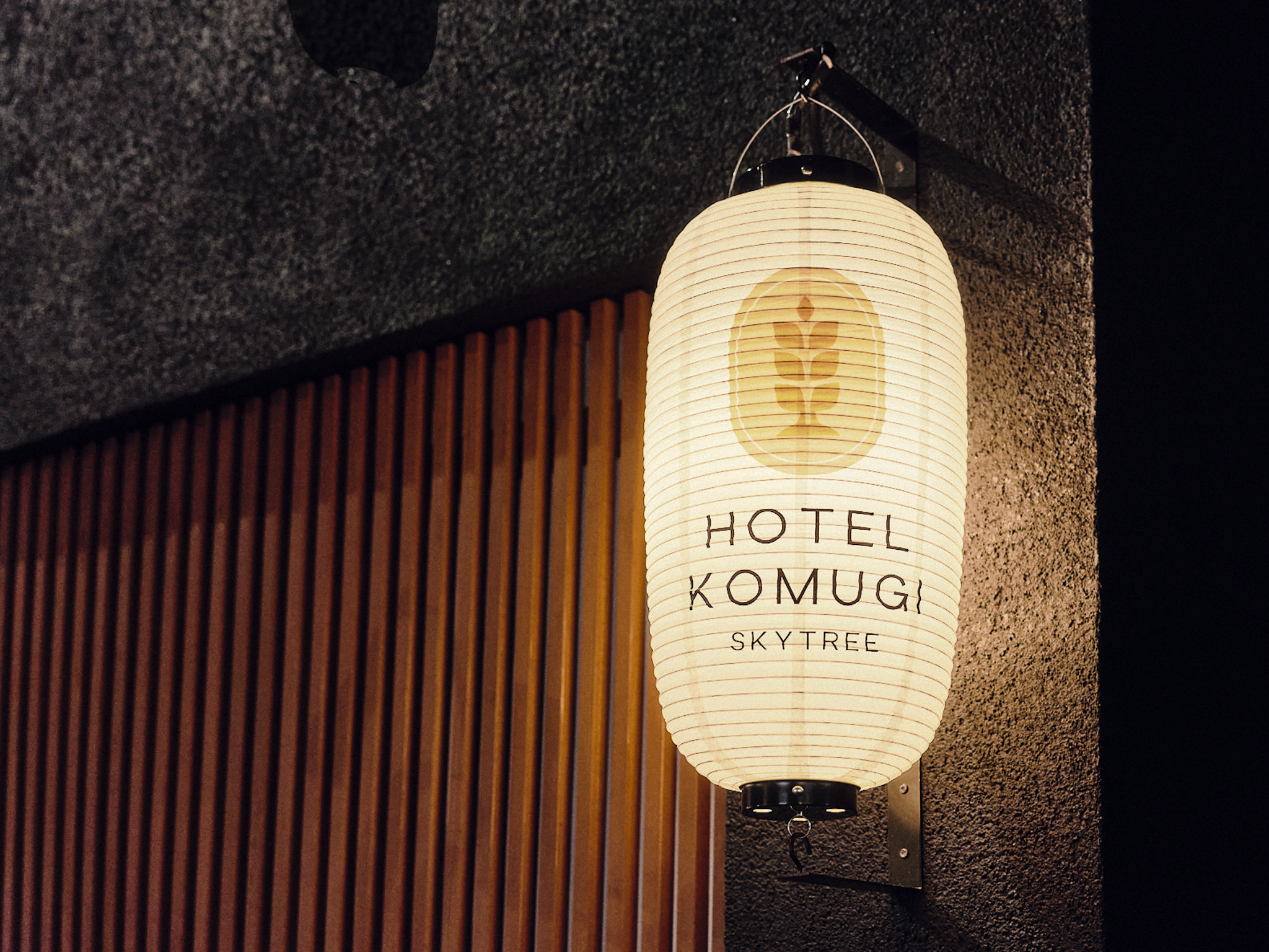 Illuminated paper lantern with the words 'Hotel Komugi Sky Tree' and a logo, mounted on a wall inside a building.