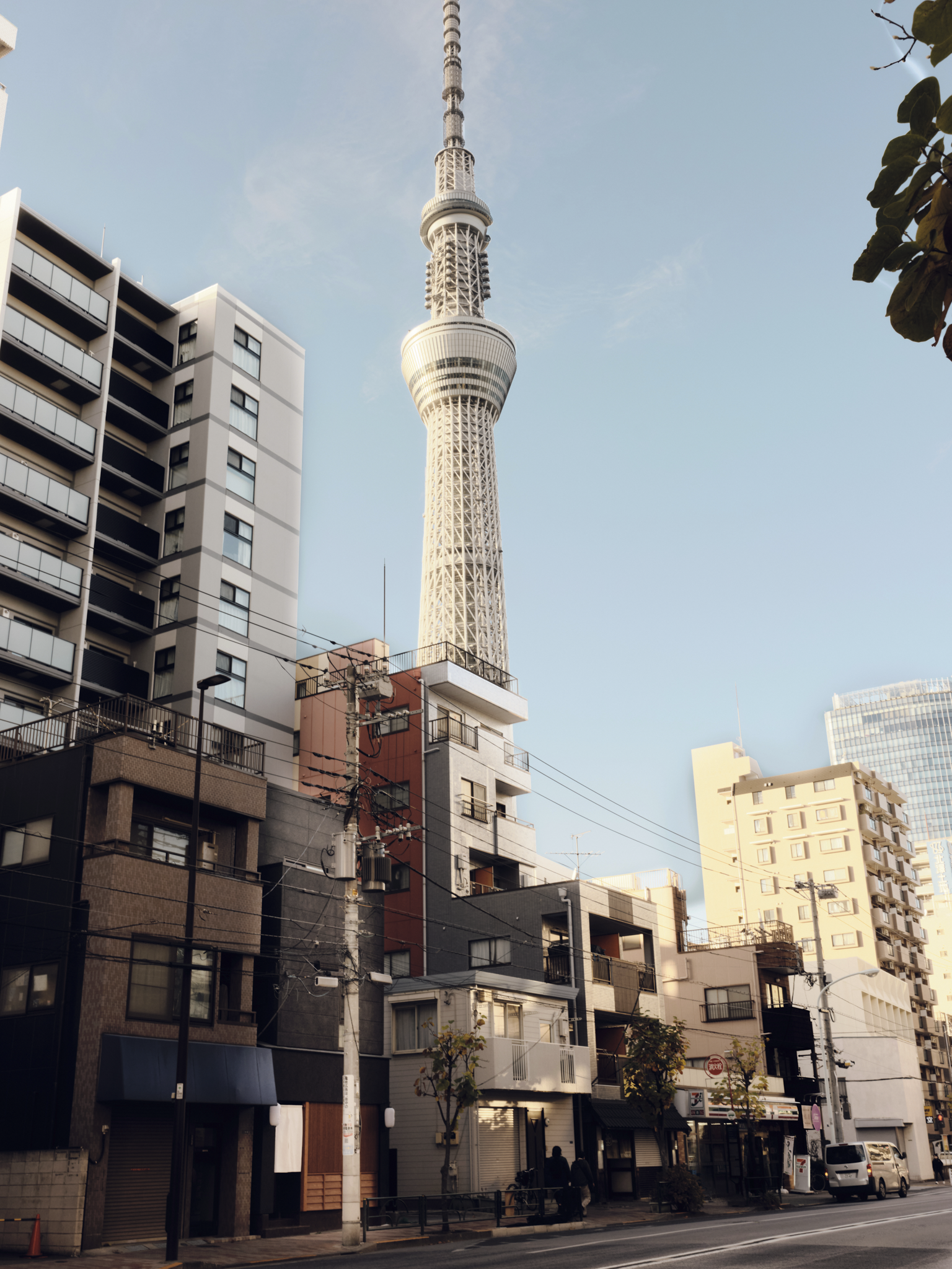City street with various buildings in the foreground, and the Tokyo Skytree tower in the background against a clear sky.